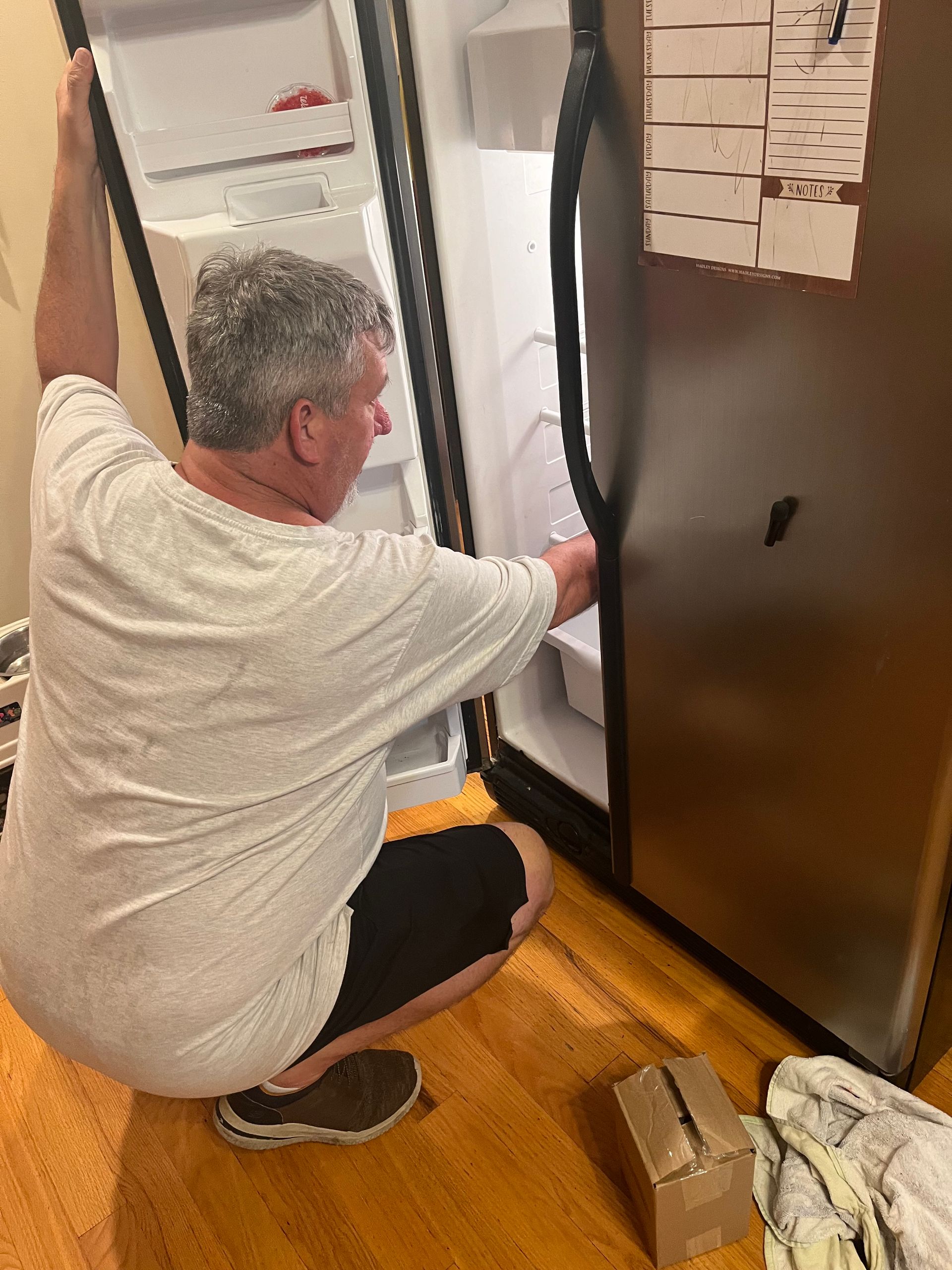A man is fixing a refrigerator in a kitchen.