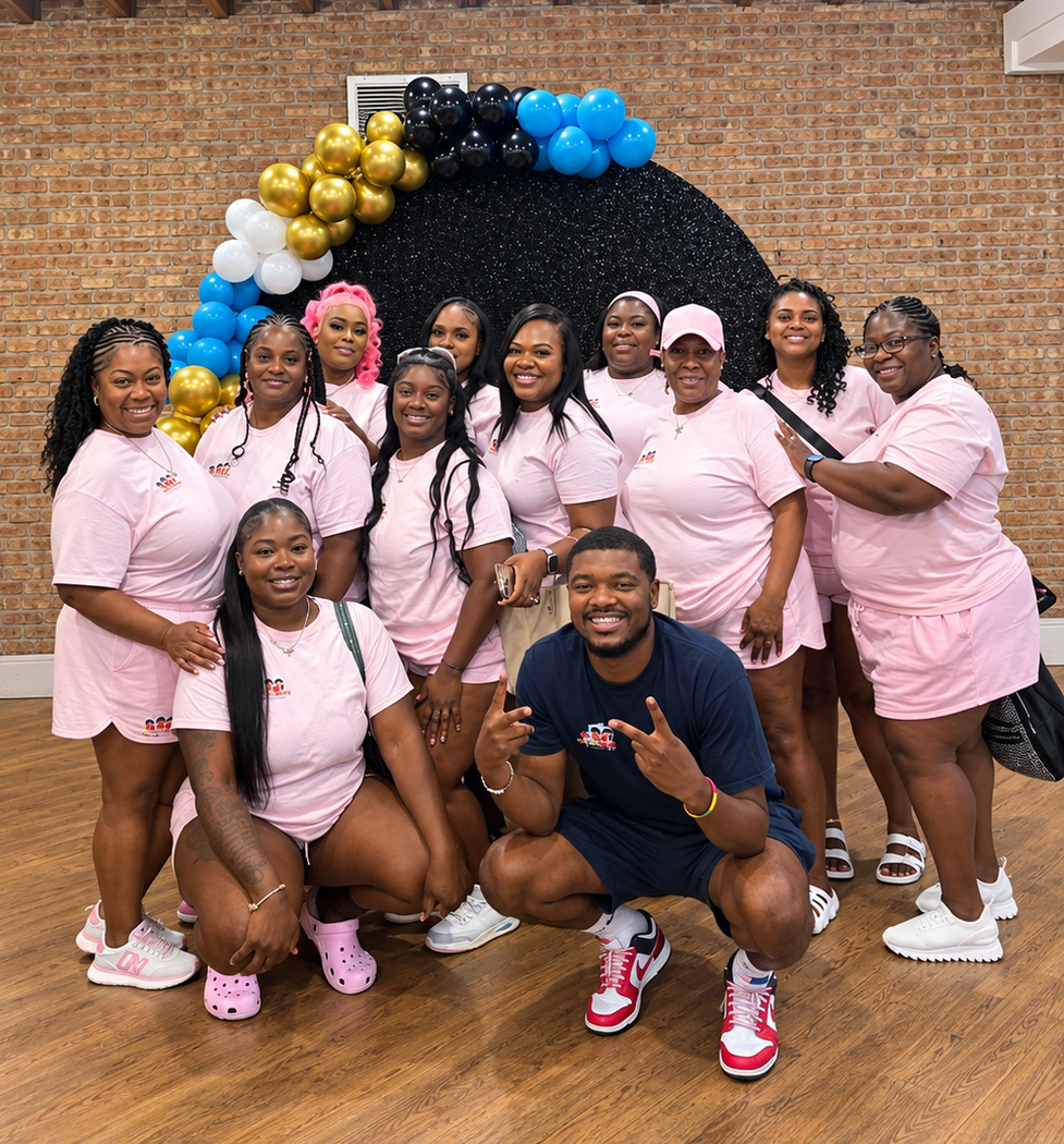 humbled hearts staff posing indoors under a gold-and-blue balloon arch, wearing pink outfits, smiling for a celebration photo
