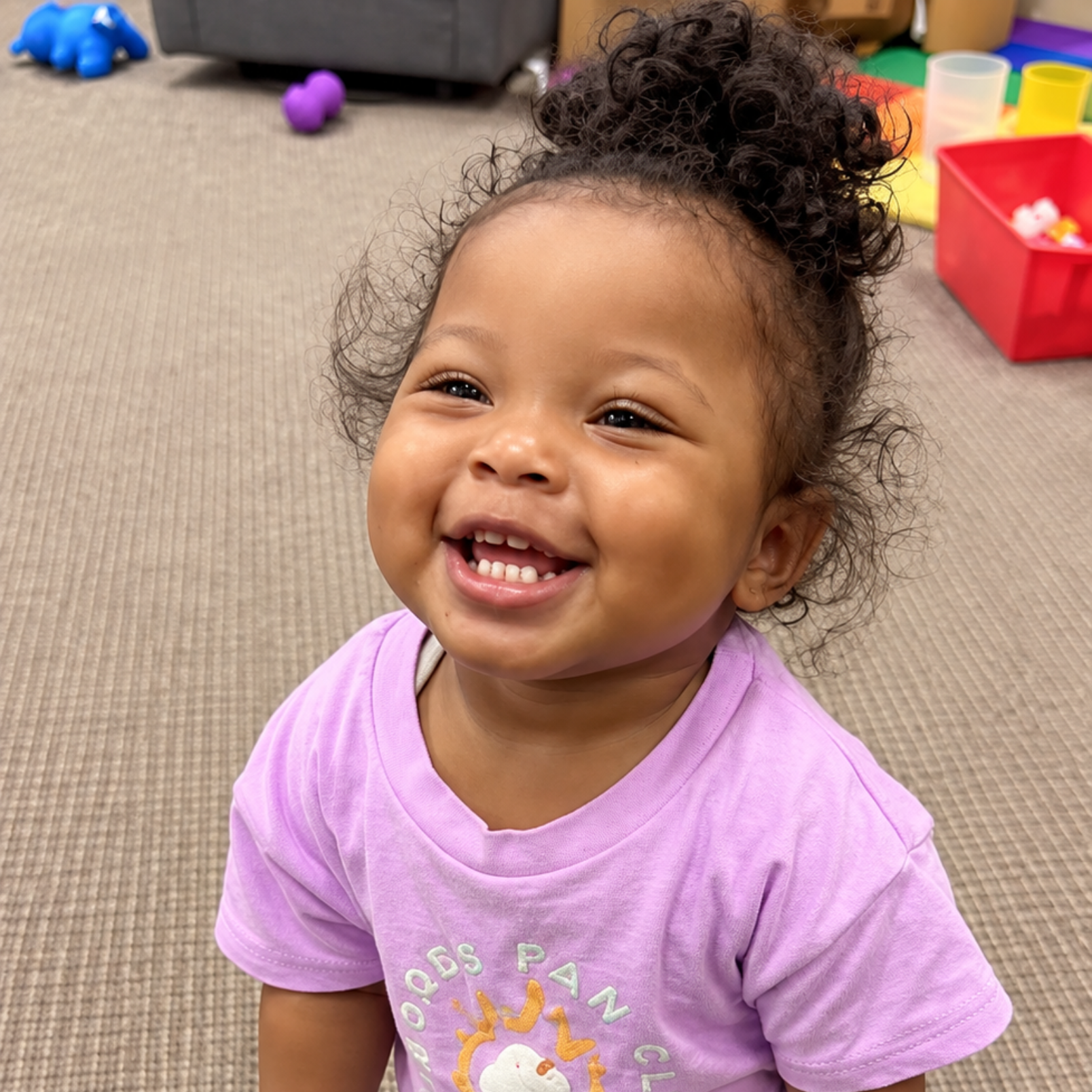 Smiling child in a purple shirt in a playroom with toys in the background