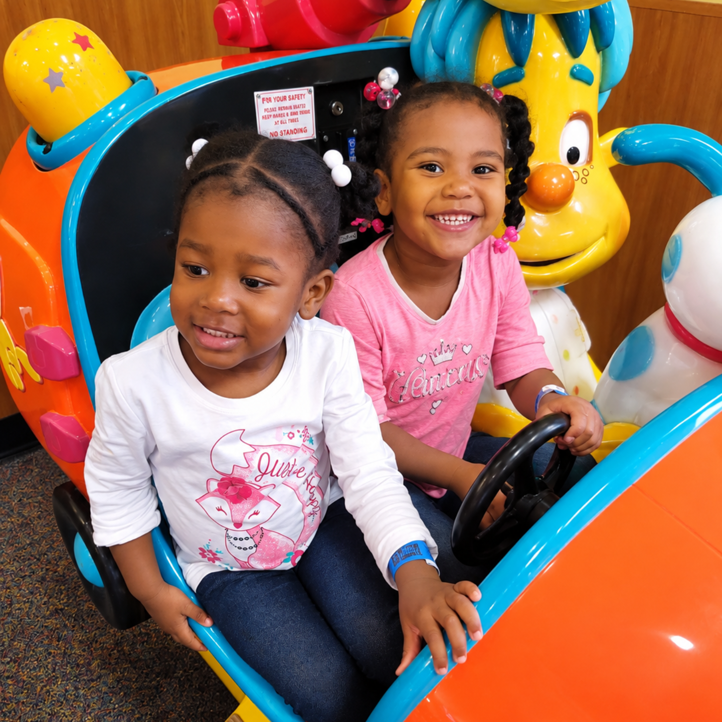 Two children smiling in a colorful amusement ride car
