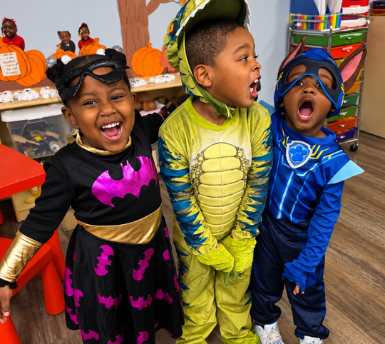 Three children in colorful costumes laughing at a Halloween party