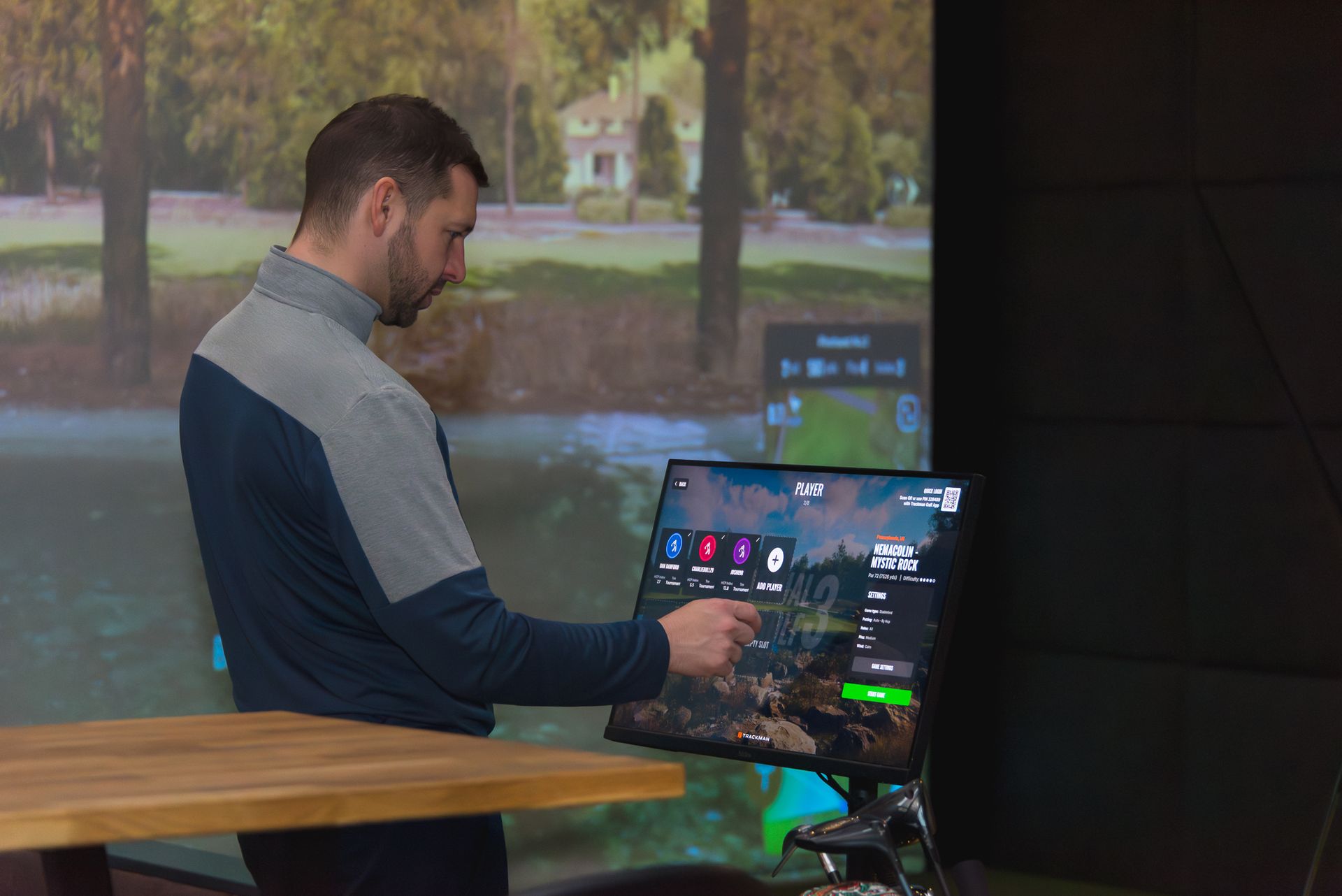 Man using a touchscreen display beside a projected outdoor scene in a dim room
