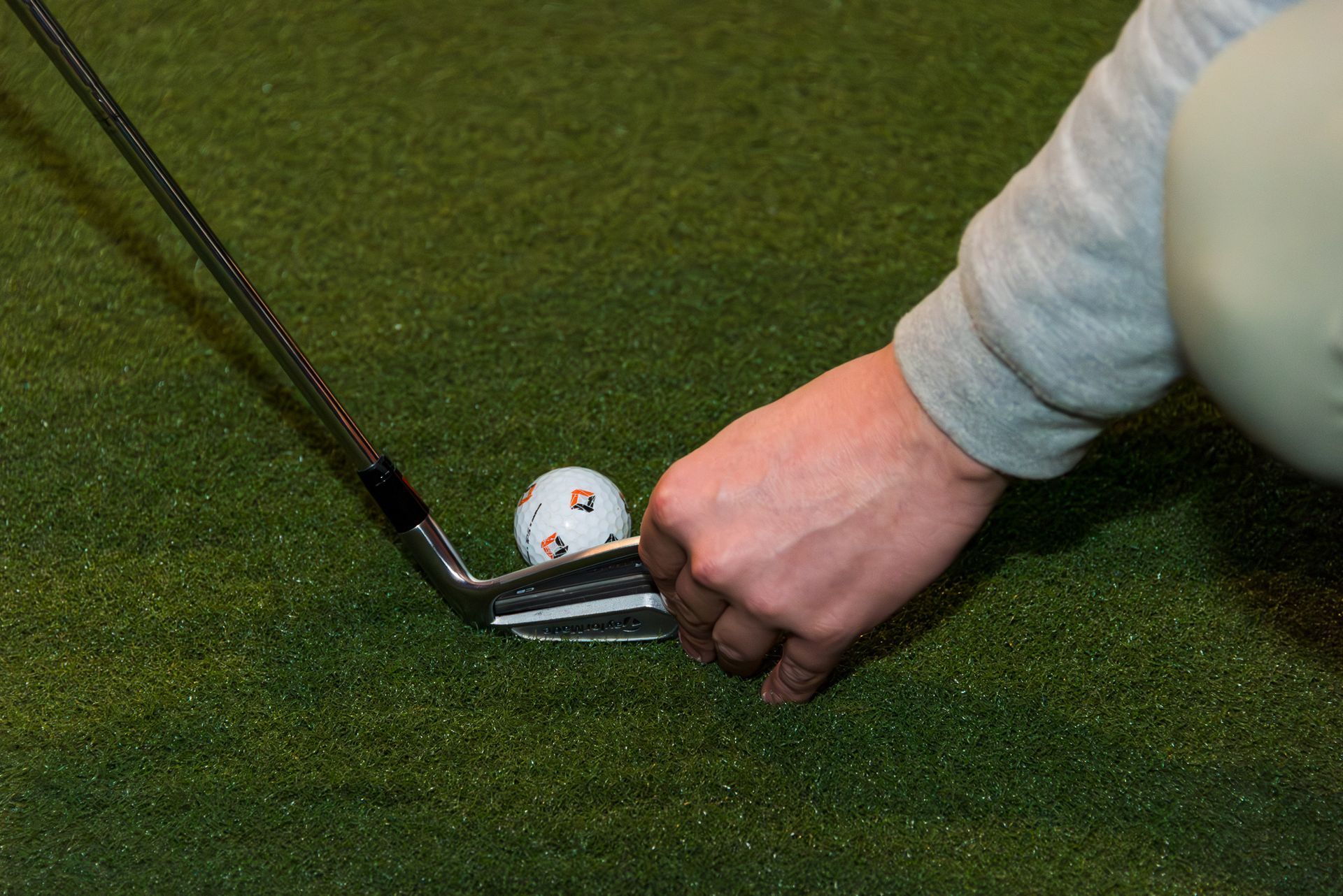 Hand placing a golf club near a golf ball on green turf