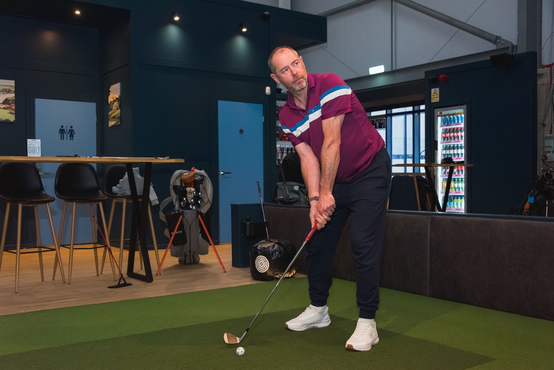Golfer in burgundy shirt practicing a putt indoors on a green turf area
