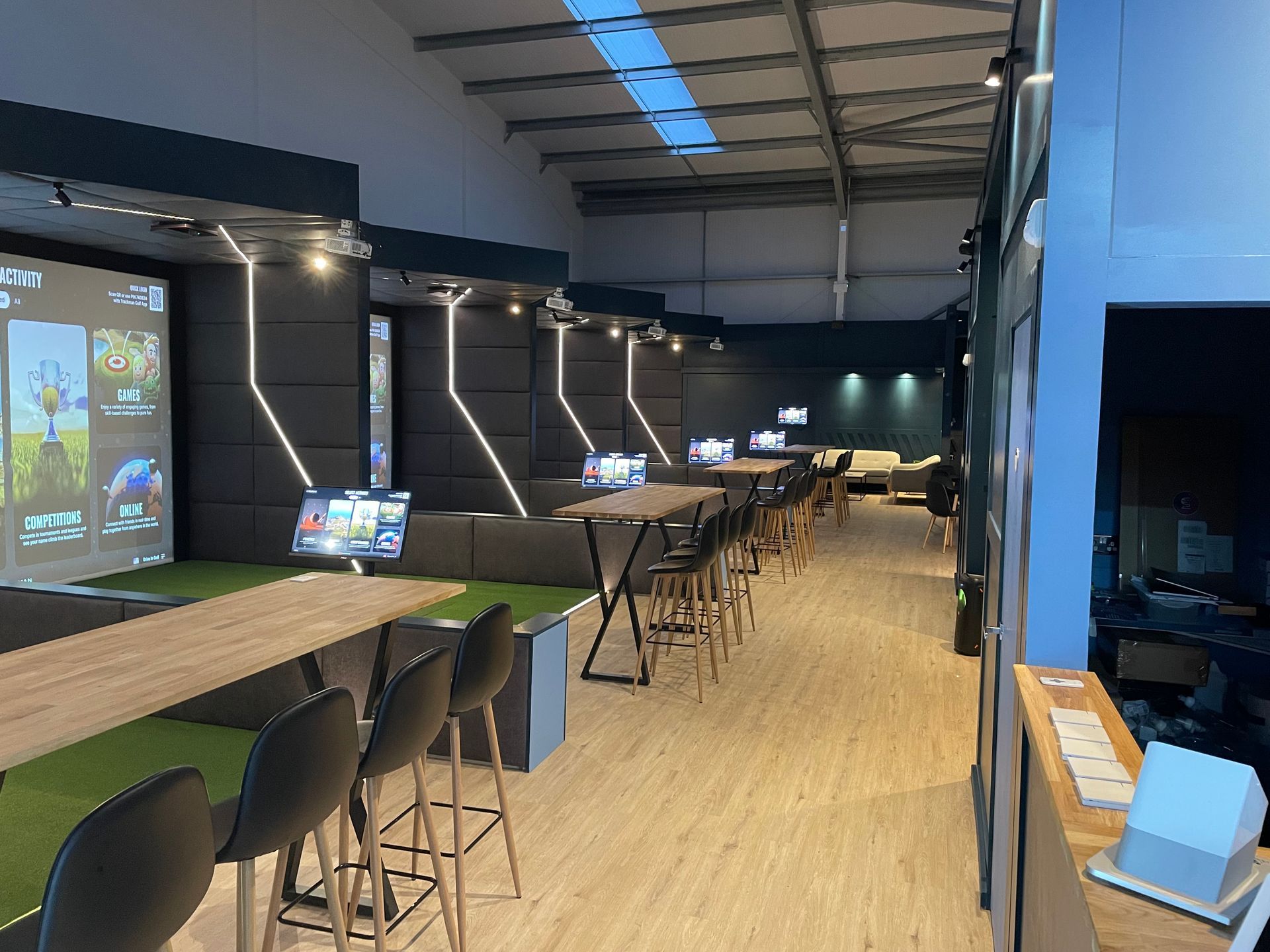 Modern indoor lounge with long tables, stools, and blue accent lighting in a spacious warehouse-style room