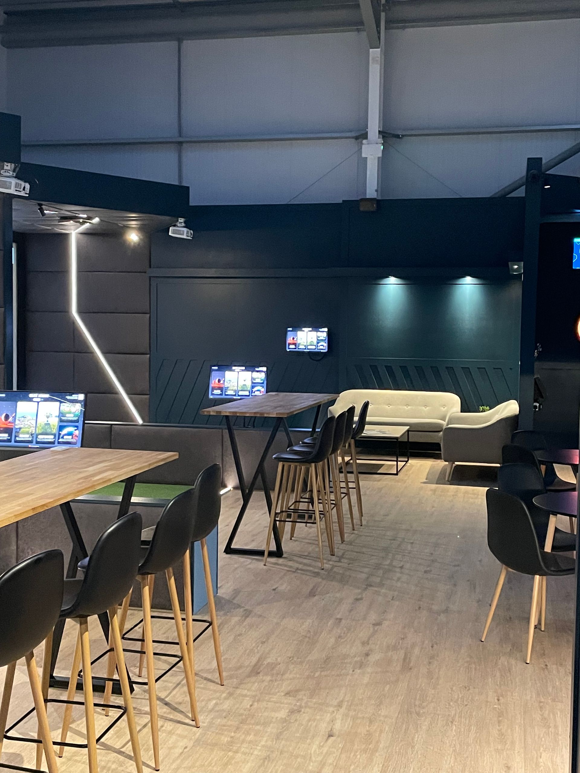 Modern bar/lounge interior with high tables, stools, wall TVs, and soft overhead lighting