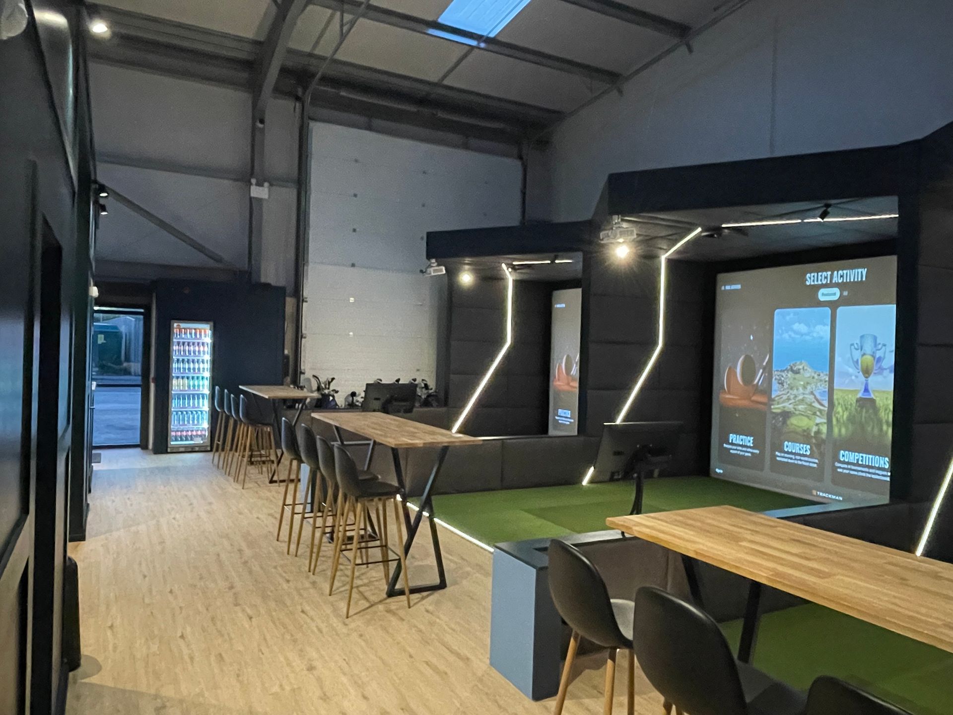 Modern indoor event space with stage, screen, tables, chairs, and open industrial ceiling