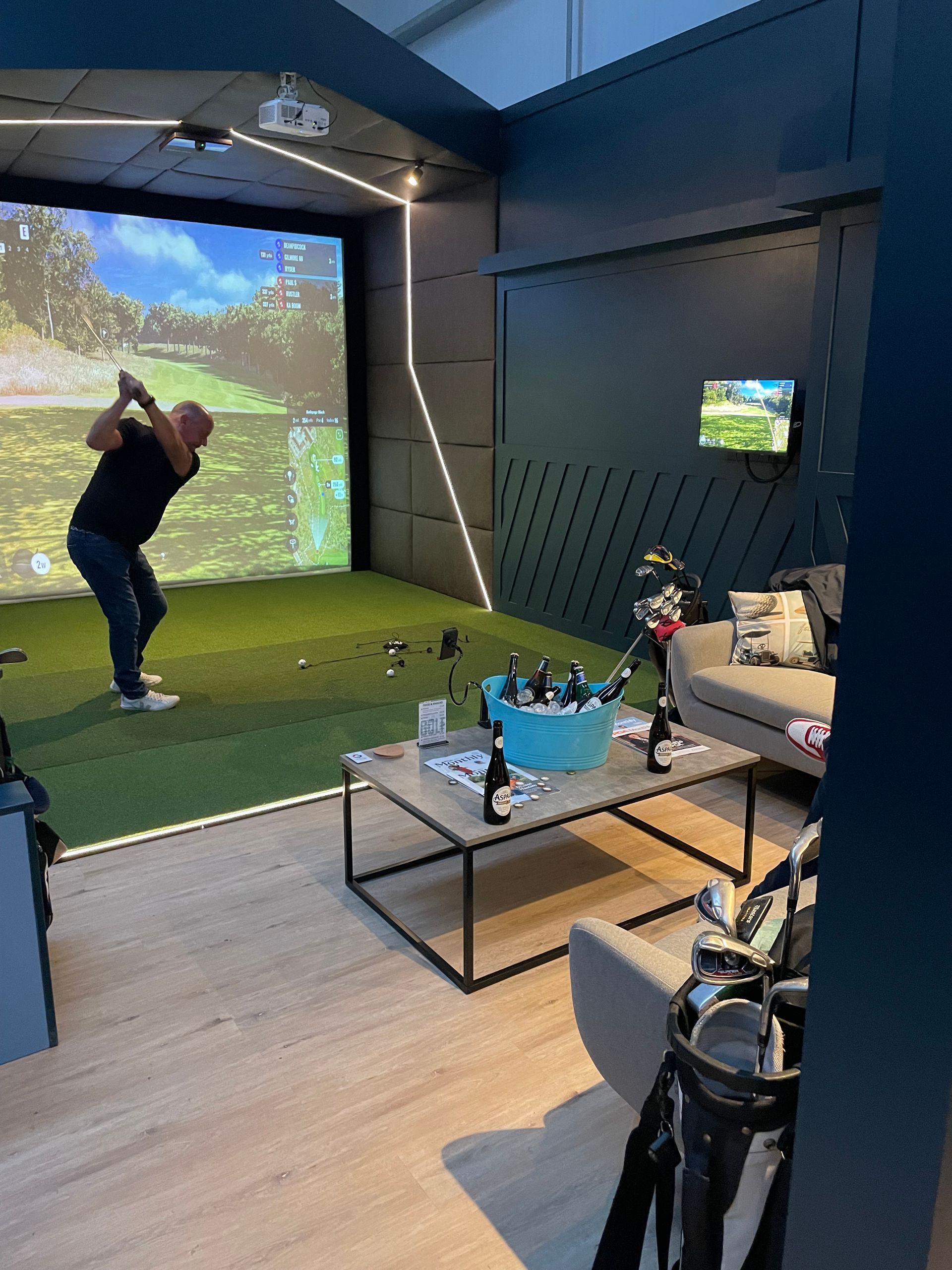 Person swinging a golf club in an indoor golf simulator room with a projected course screen