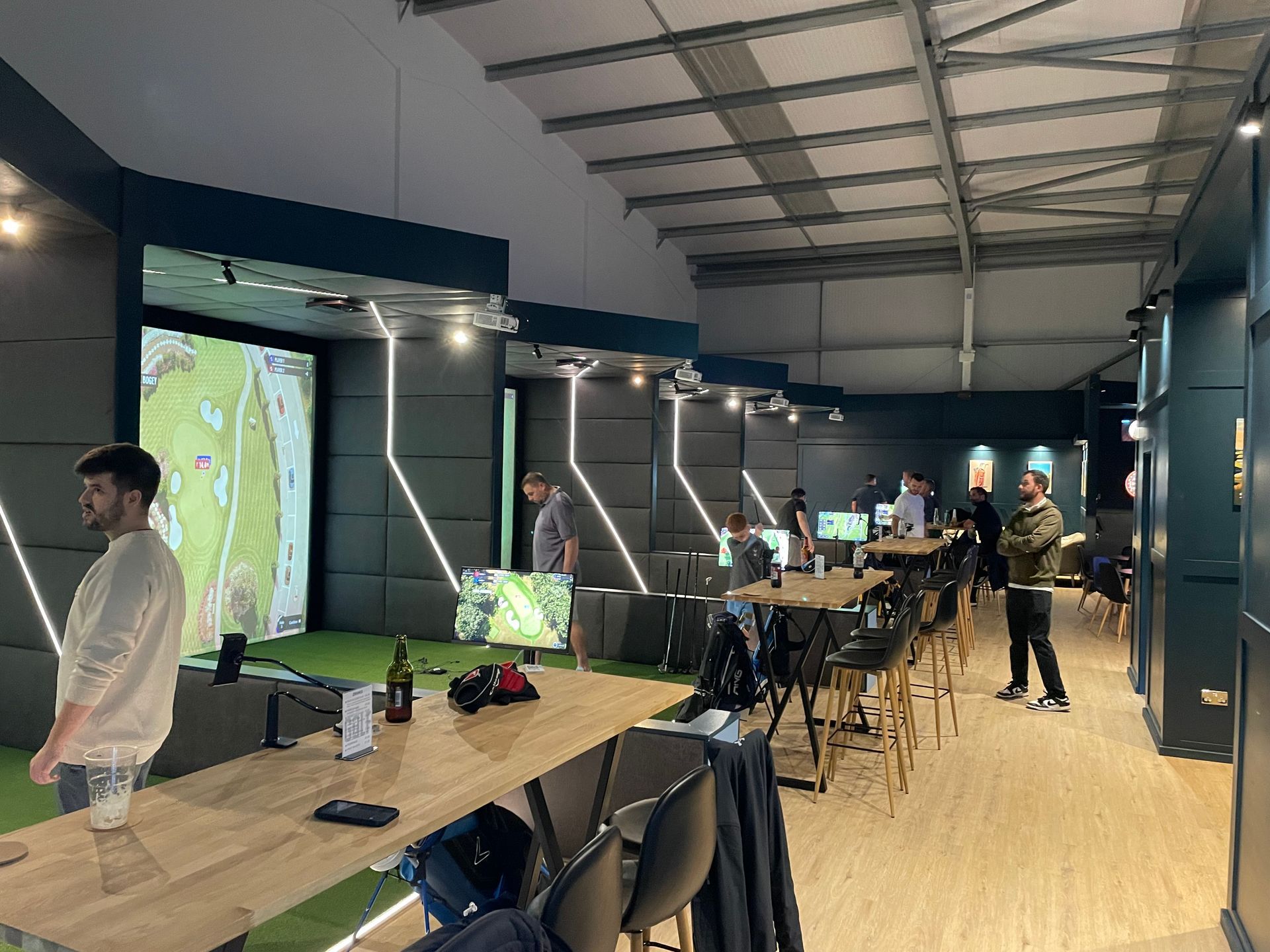 Indoor event space with large projection screens, tables, and people gathered around a demonstration setup