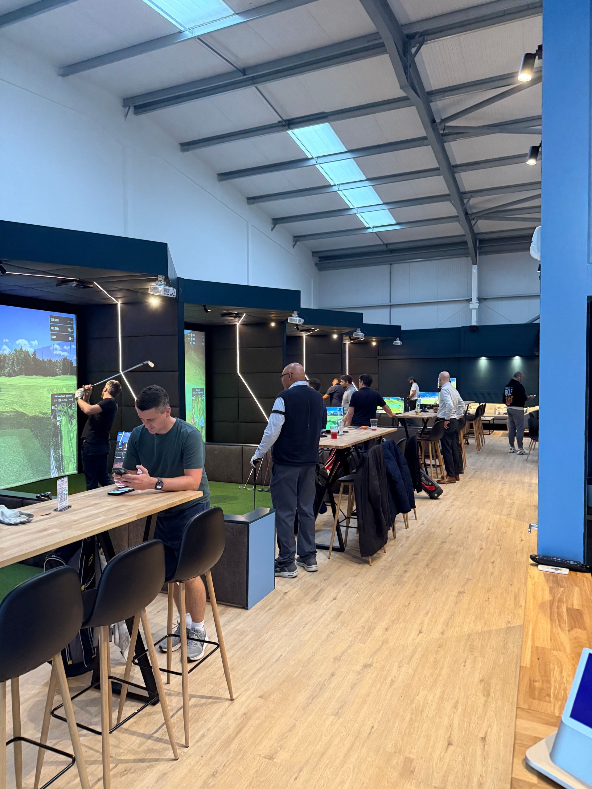 Bright coworking space with people working at tables and a large screen on the left