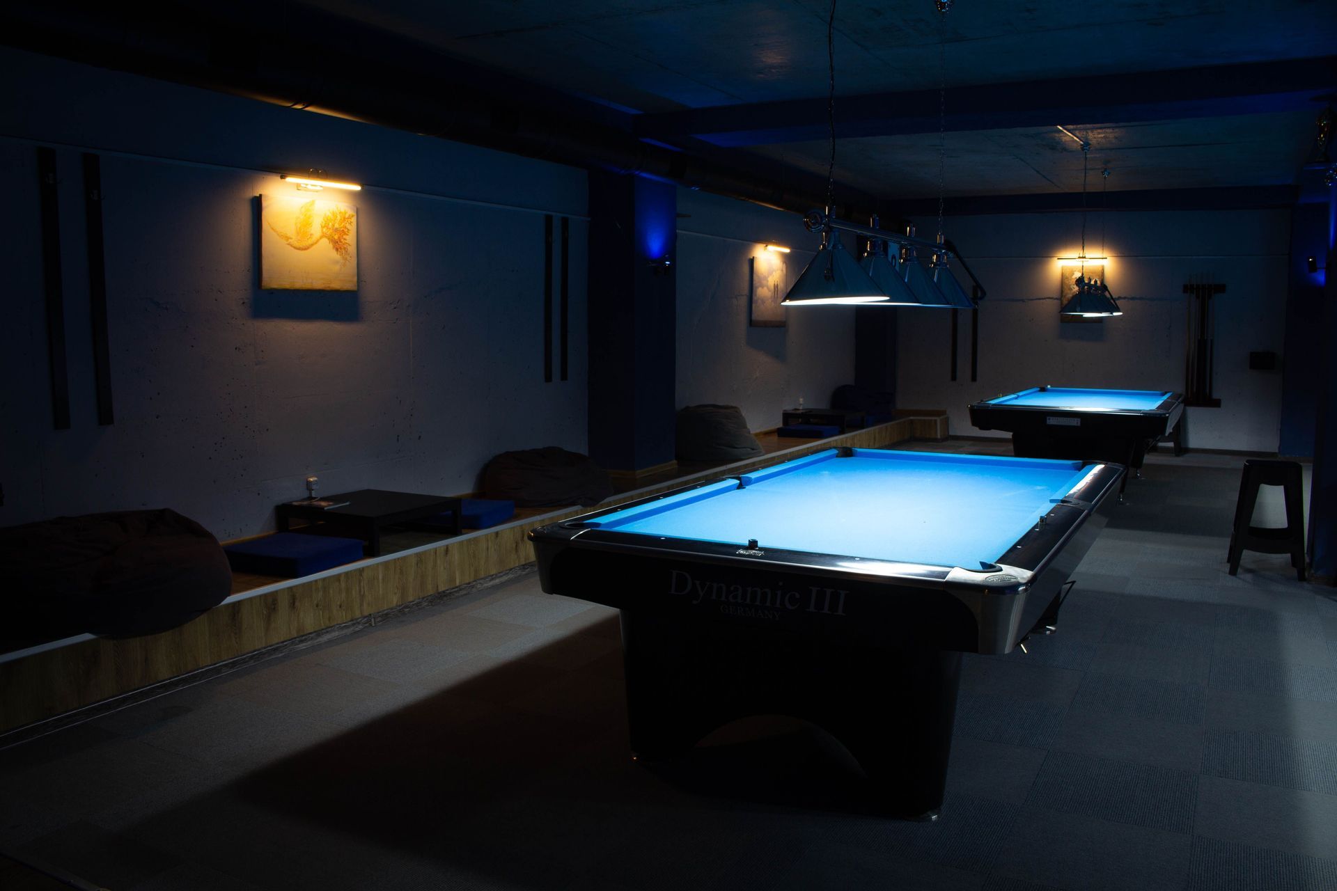 Dim billiards room with blue-felt pool tables and wall-mounted lights