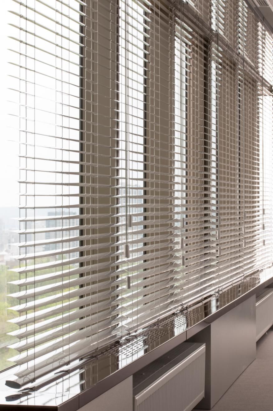 Office windows with partially closed blinds, sunlight filtering through, and radiators below