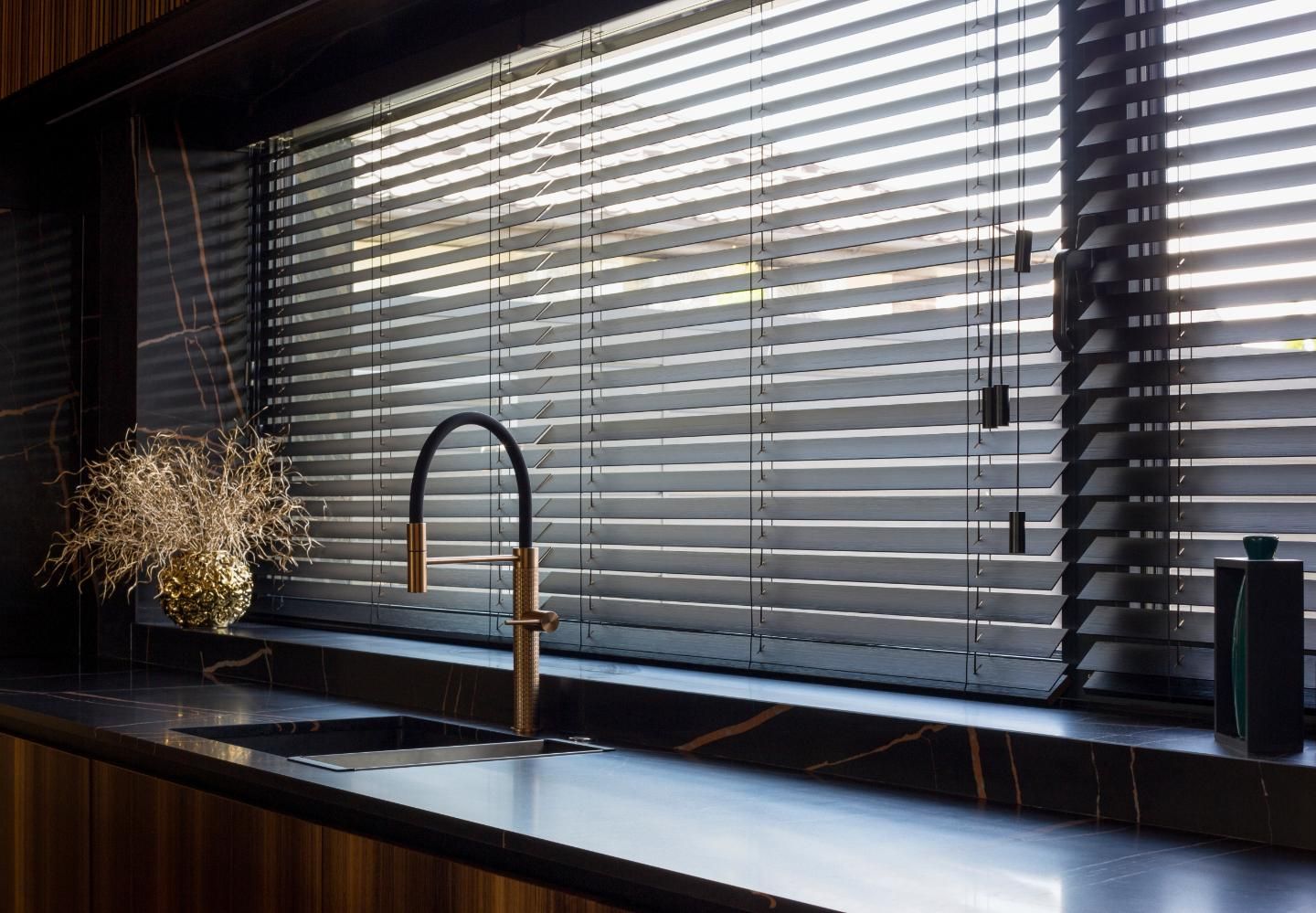 Modern kitchen sink by a window with dark blinds and a potted plant on the counter