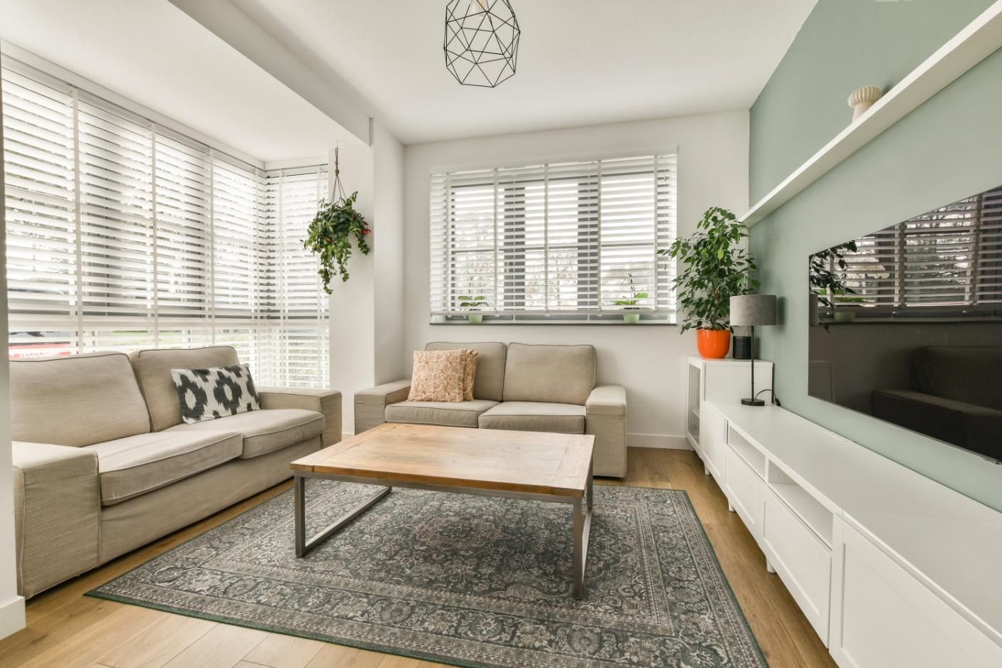 Bright living room with beige sofas, coffee table, large rug, window blinds, and wall-mounted TV