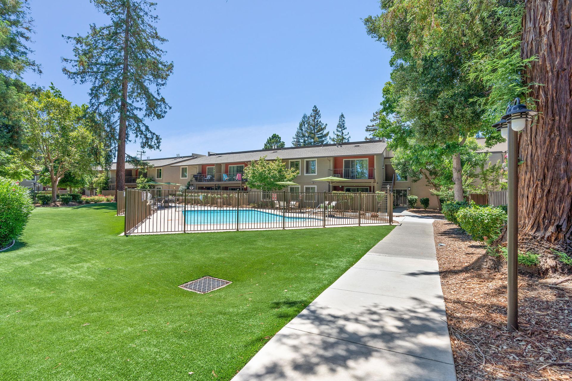 Outdoor community pool area with a fence, lounge chairs, and surrounding apartment buildings.