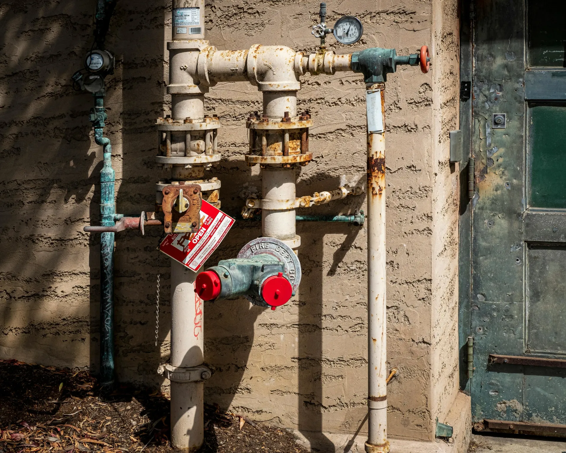 Outdoor gas meter and pipes mounted on a weathered wall with red valve handles
