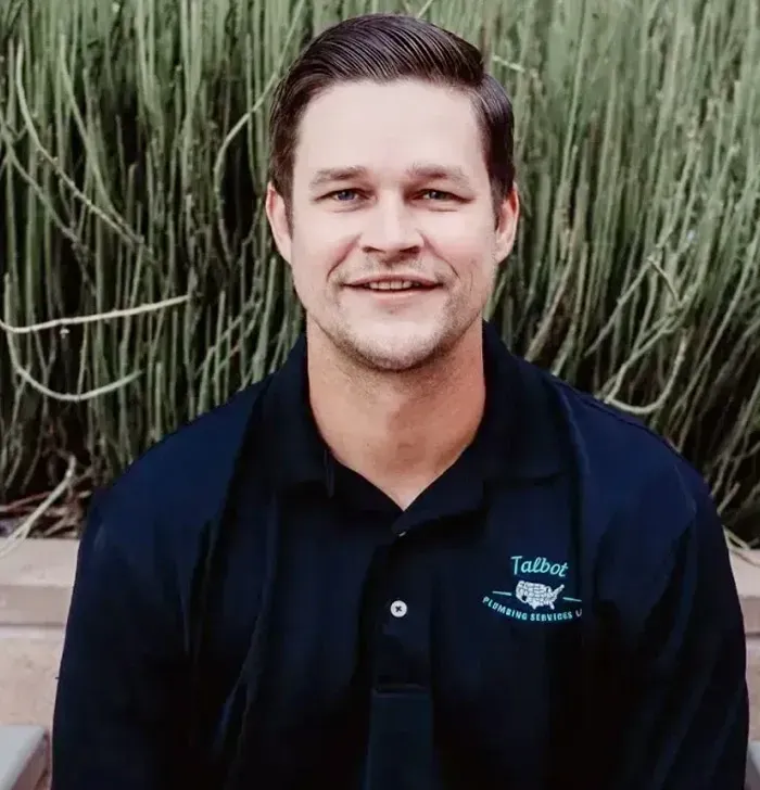 Smiling man in a navy polo shirt standing in front of tall green plants