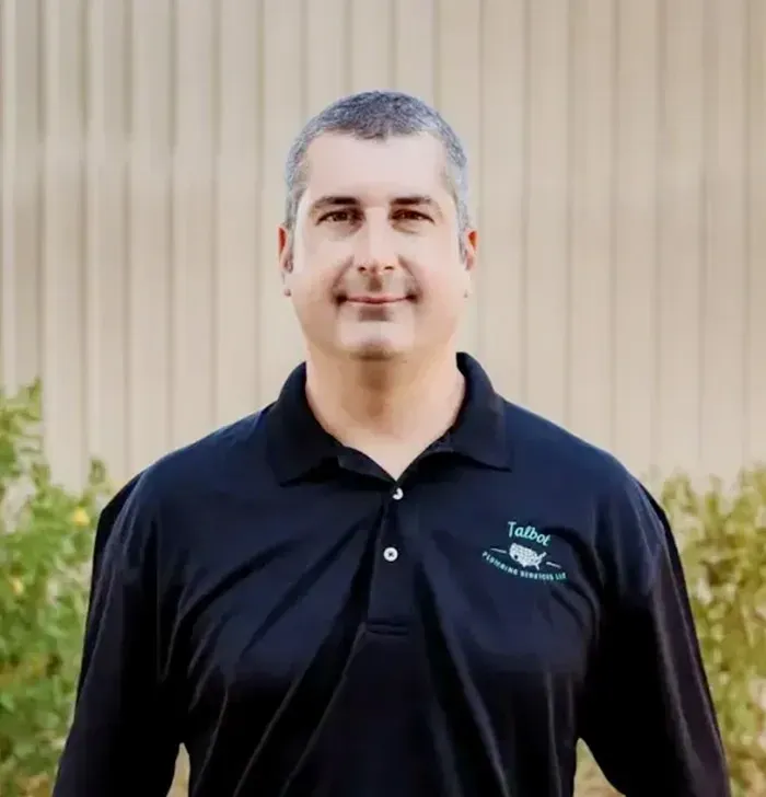 Portrait of a man in a black polo shirt standing before a beige wall