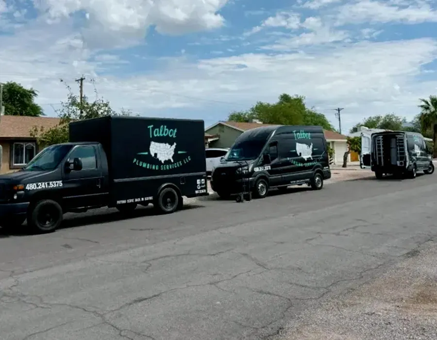 Black delivery trucks lined up on a residential street under a partly cloudy sky.