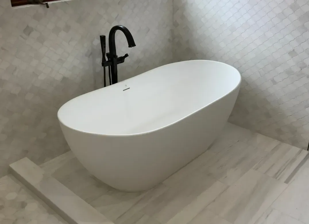 Modern bathroom with a white freestanding bathtub, black faucet, and tiled walls.