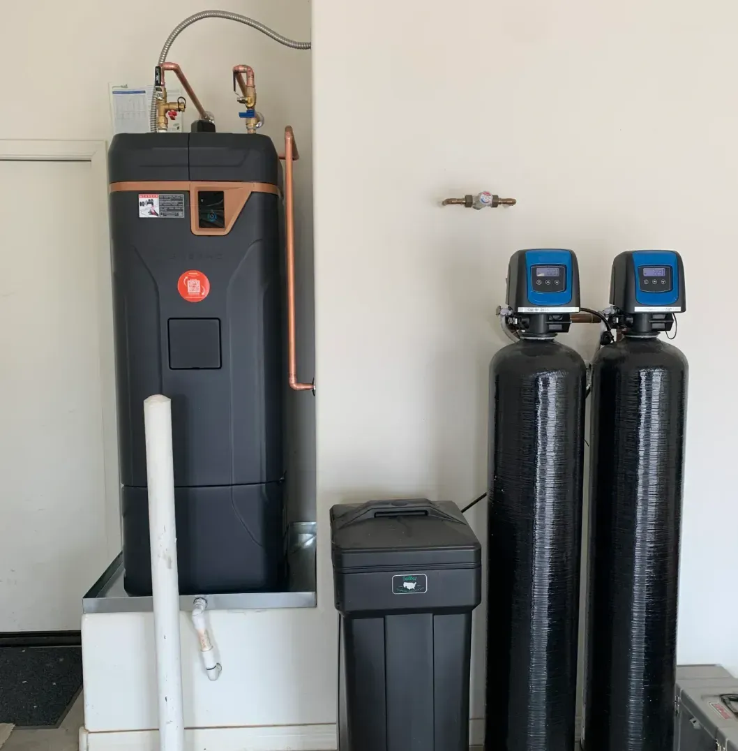 Water softener and filtration system in a utility room with black tanks and a white basin.
