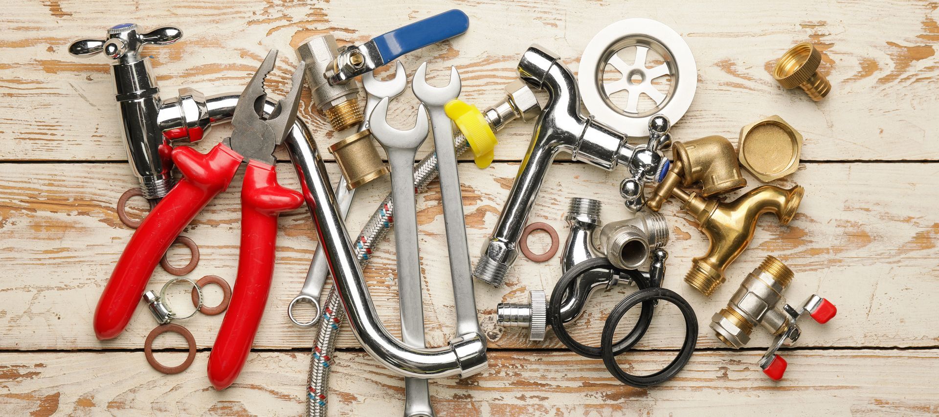Plumbing tools and pipe fittings neatly arranged on a light wooden surface.