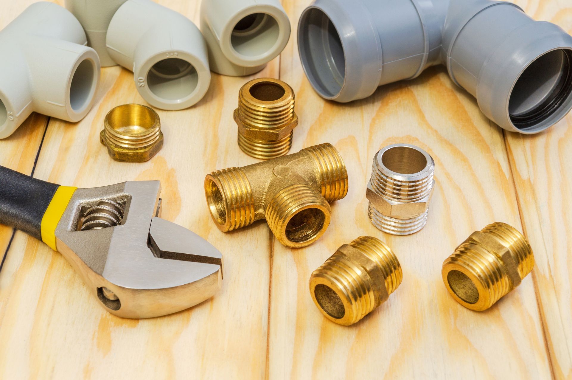 Plumbing parts and adjustable wrench on wooden surface.
