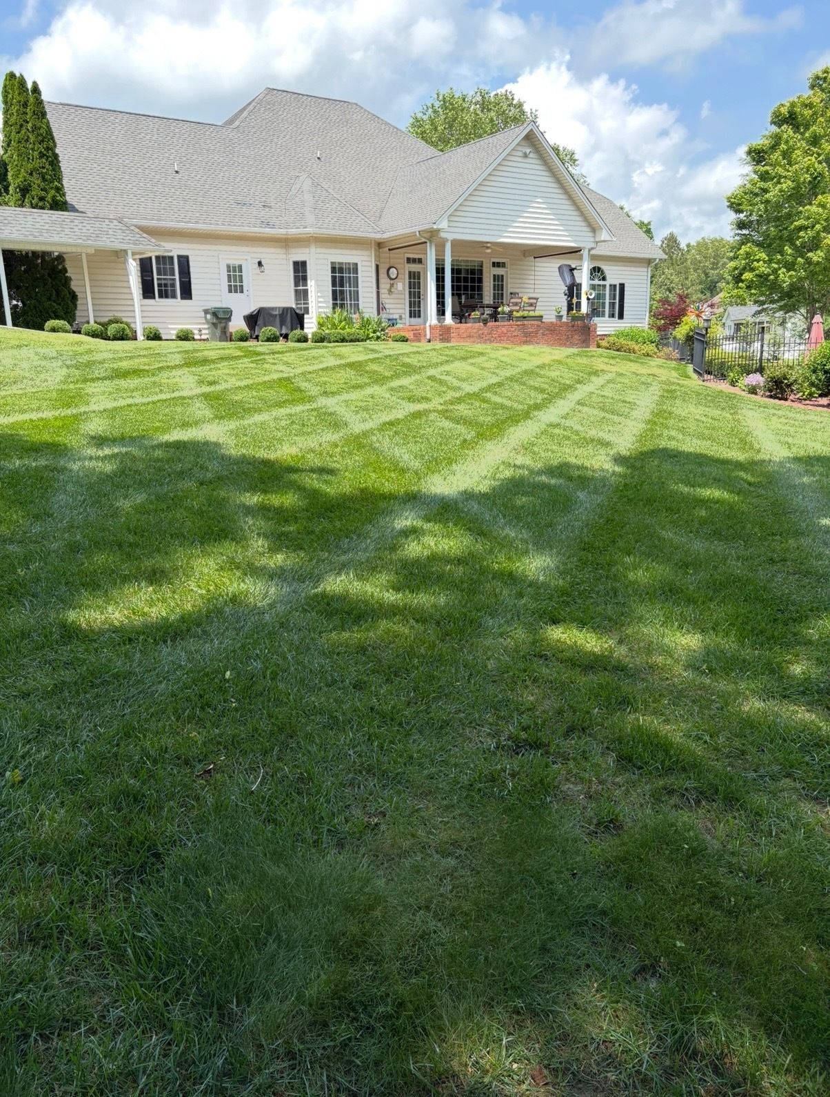 Single-story white house with a striped green lawn, flower beds, and a sunny blue sky.
