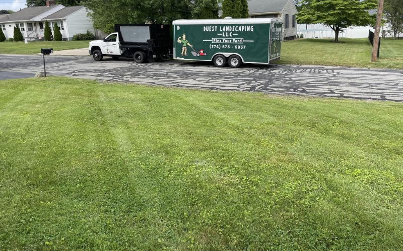 Green lawn with a landscaping truck and trailer parked on a street.