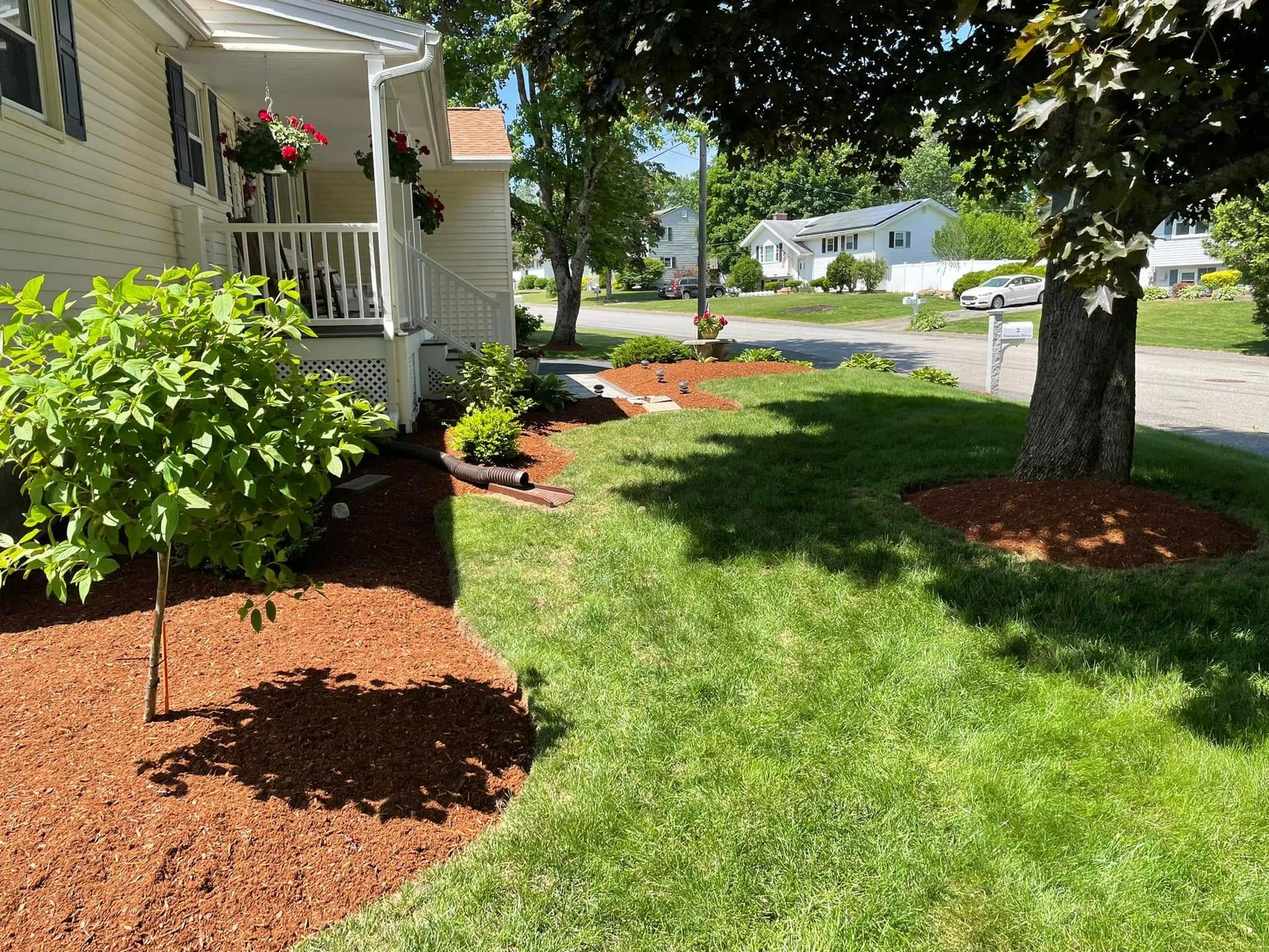 Yellow house with porch and lush green lawn with freshly mulched flowerbeds on a sunny day.