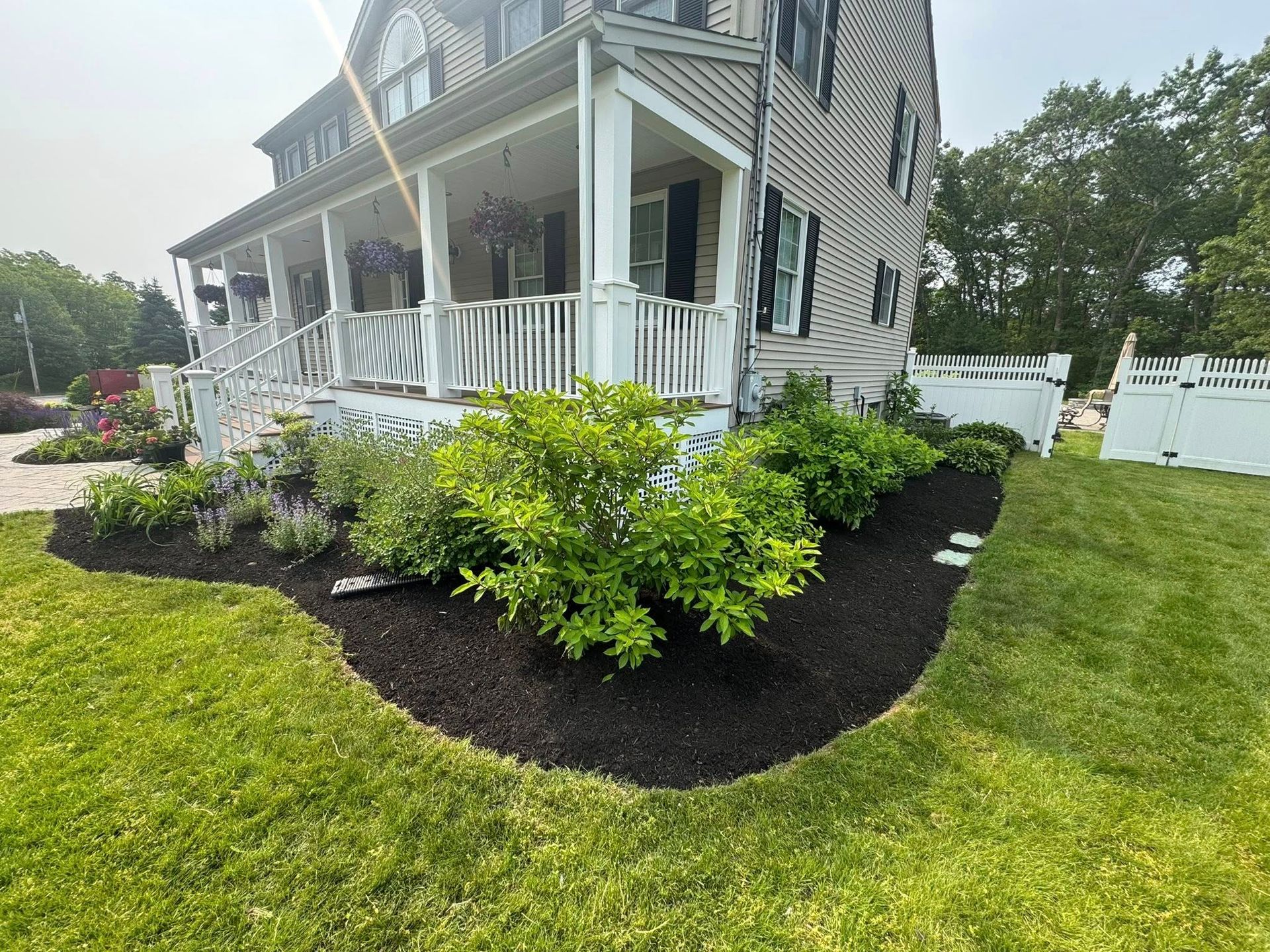 A two-story house with a porch, surrounded by freshly mulched flower beds and green grass on a sunny day.