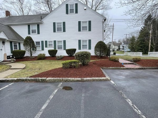 White building with green shutters, brown mulch, and a parking lot in front.