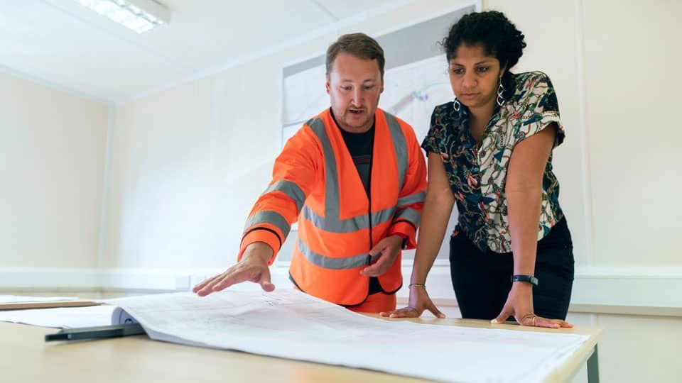 A man and a woman are looking at a blueprint on a table.