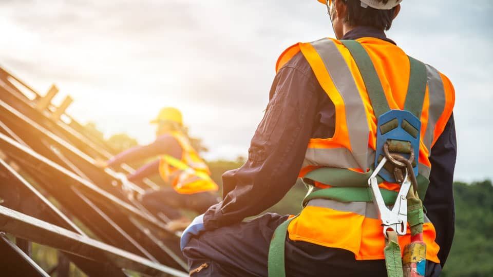 A construction worker wearing a safety harness is sitting on a roof.