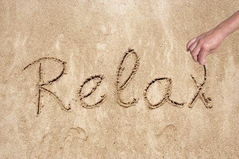 the word 'relax' being written on sand in cursive using a finger.