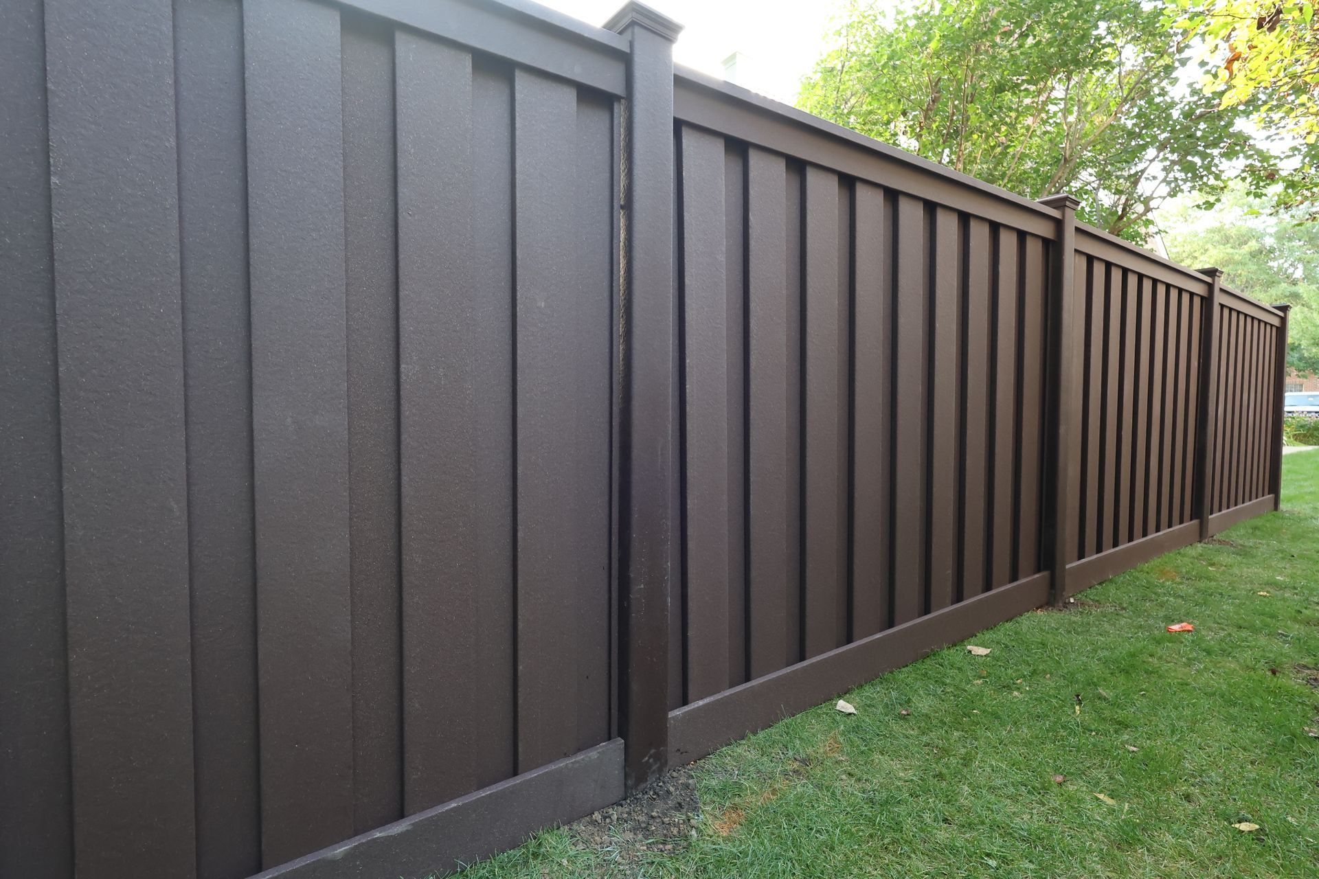 A brown composite fence is sitting on top of a lush green lawn.