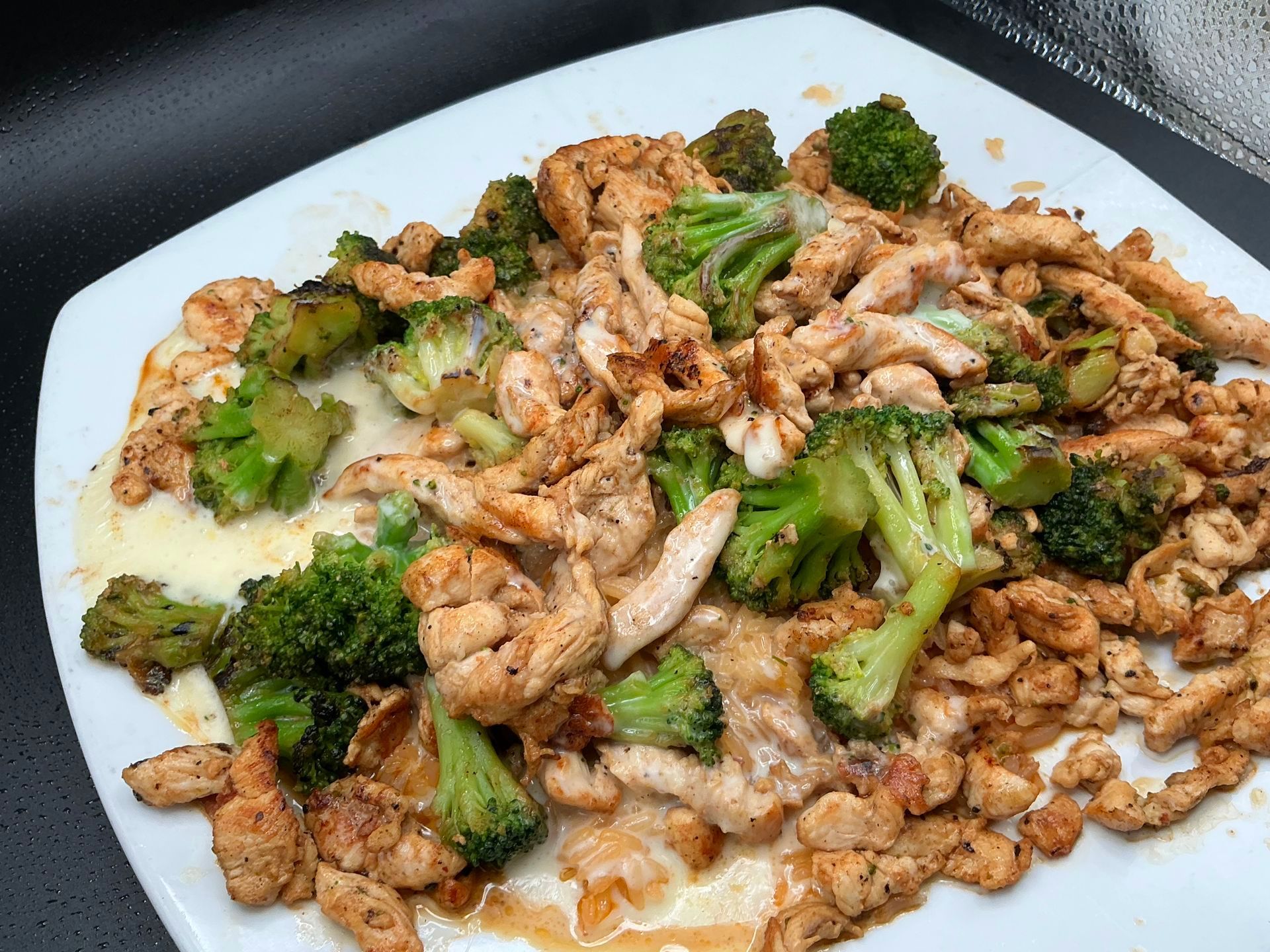 Chicken and broccoli on a white plate. Chicken is shredded and seasoned. Broccoli florets are bright green.
