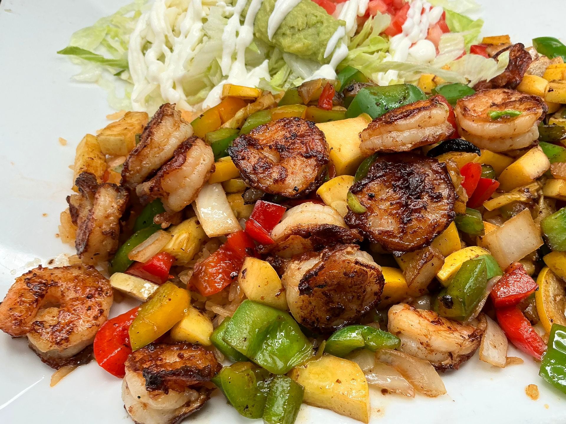 Seared shrimp with sautéed peppers and mango, served with a side salad topped with dressing.