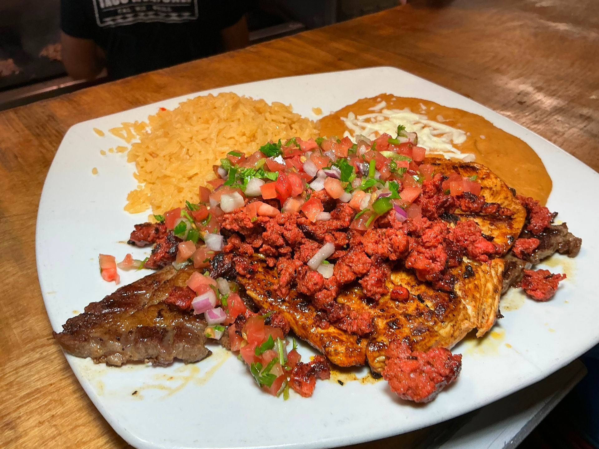 Plate of Mexican food: grilled steak and chicken topped with chorizo and pico de gallo, with rice and refried beans.
