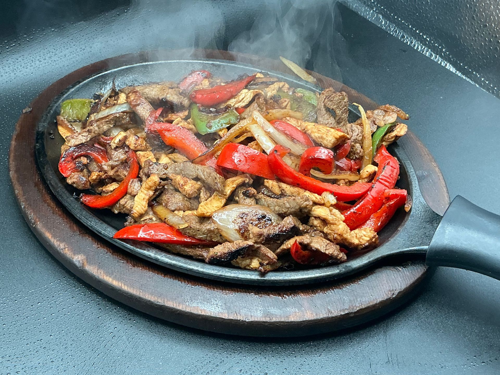 Sizzling fajitas on a hot skillet, with red and green bell peppers, onions, and meat, steaming.