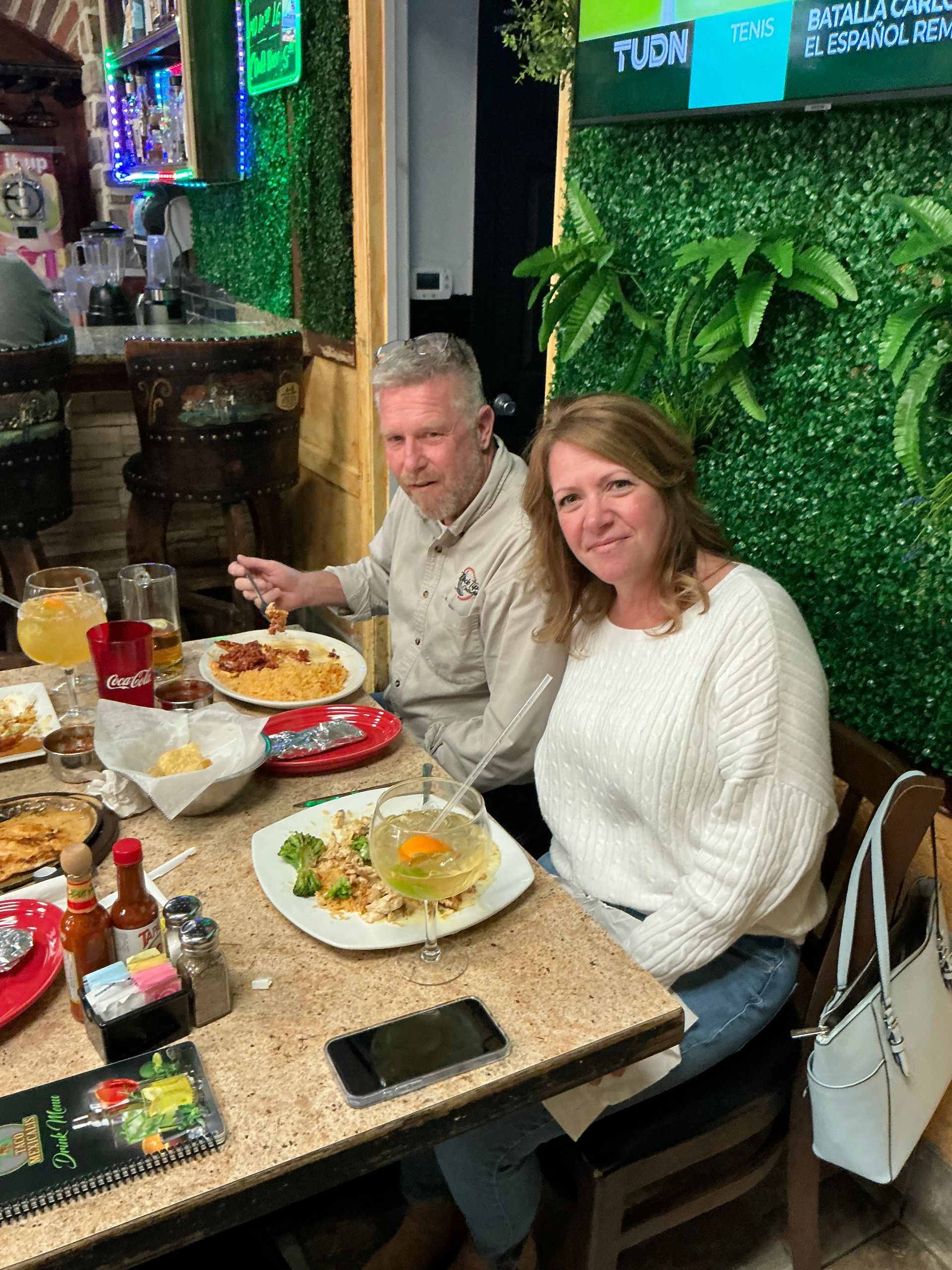 Couple dining in a restaurant with food on the table, seated near a green wall.