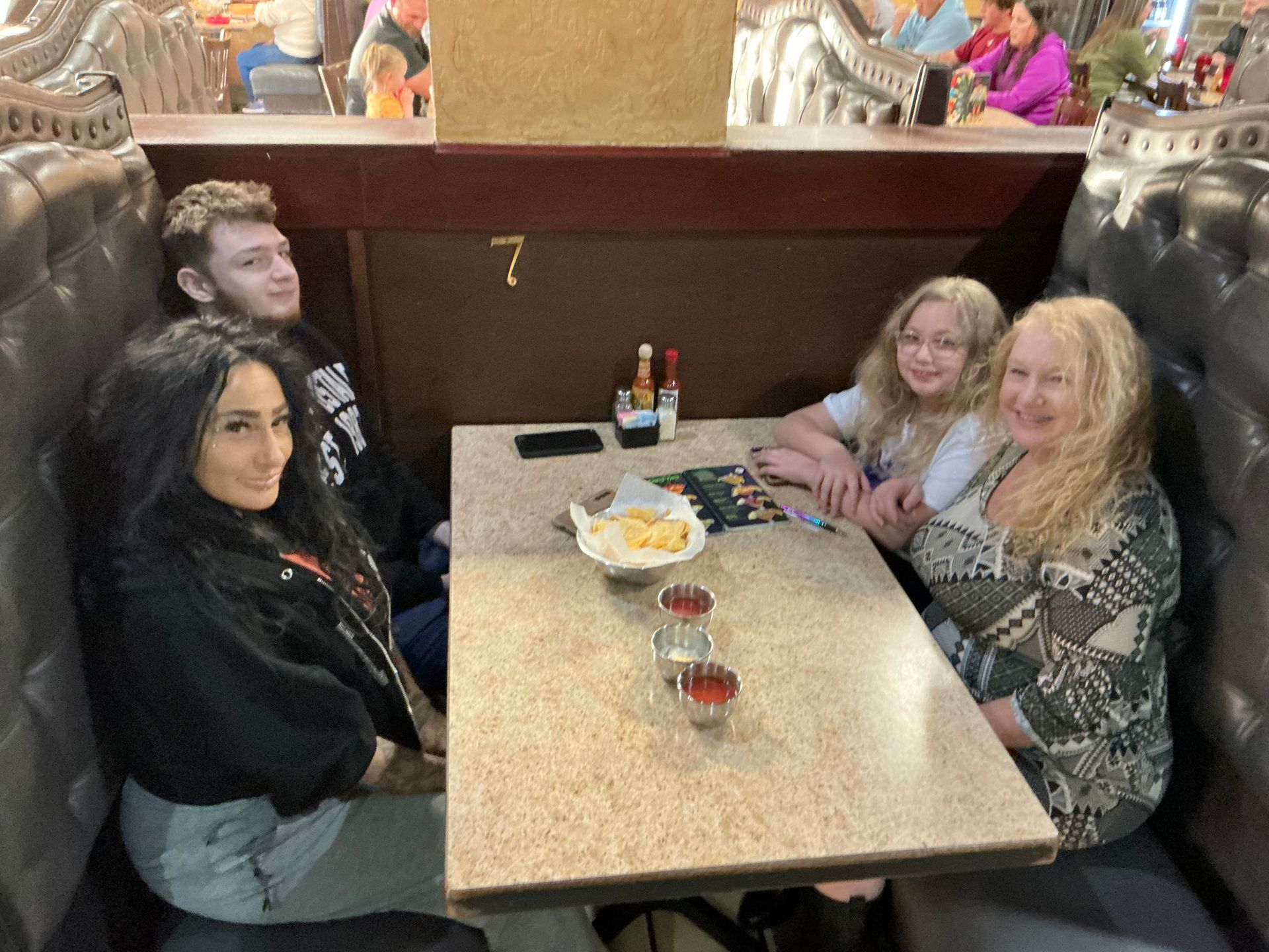 Four people seated at a booth in a restaurant. They are smiling and looking at the camera.