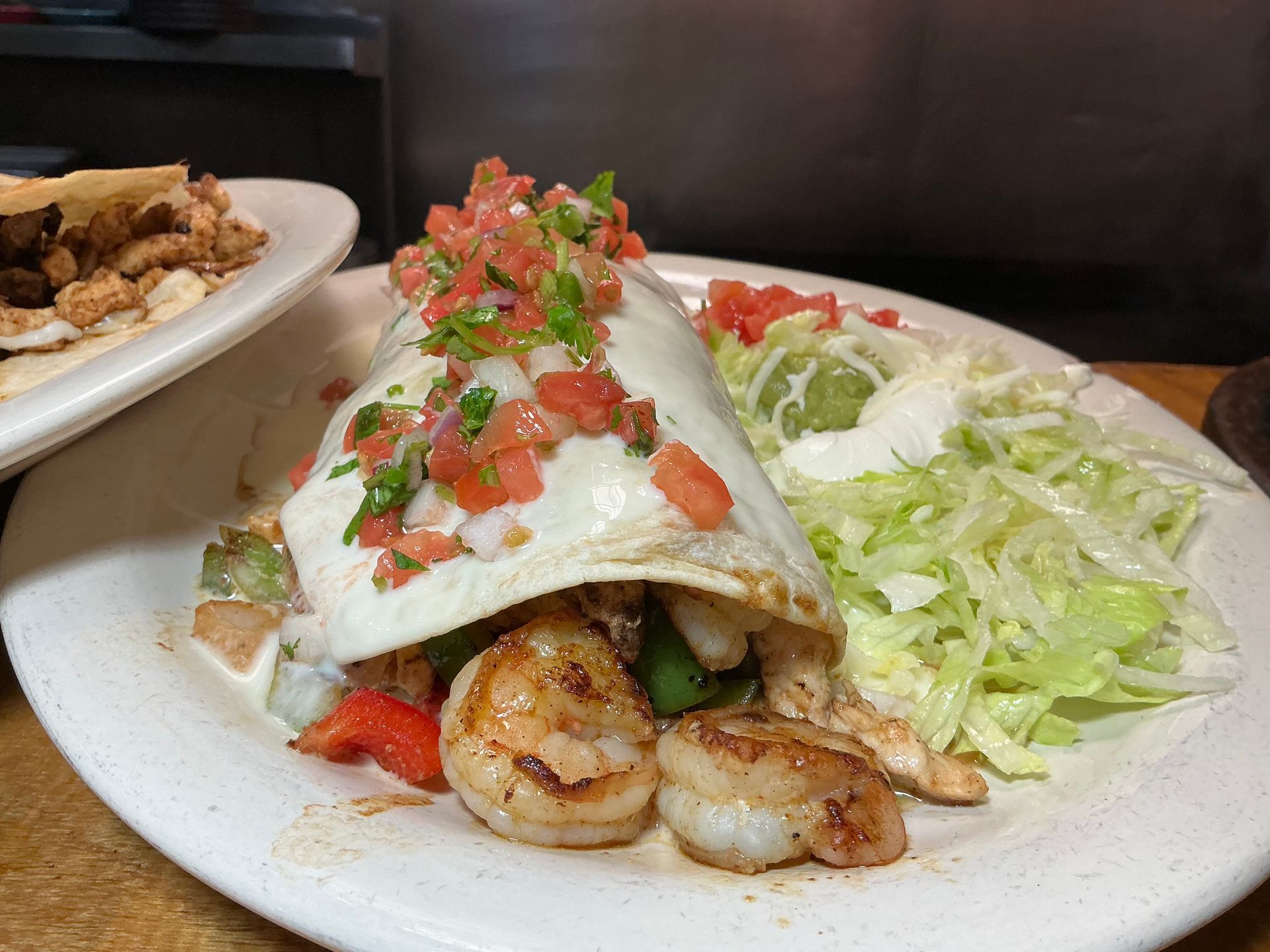 Burrito topped with salsa and cheese, served with lettuce, guacamole, and sour cream.