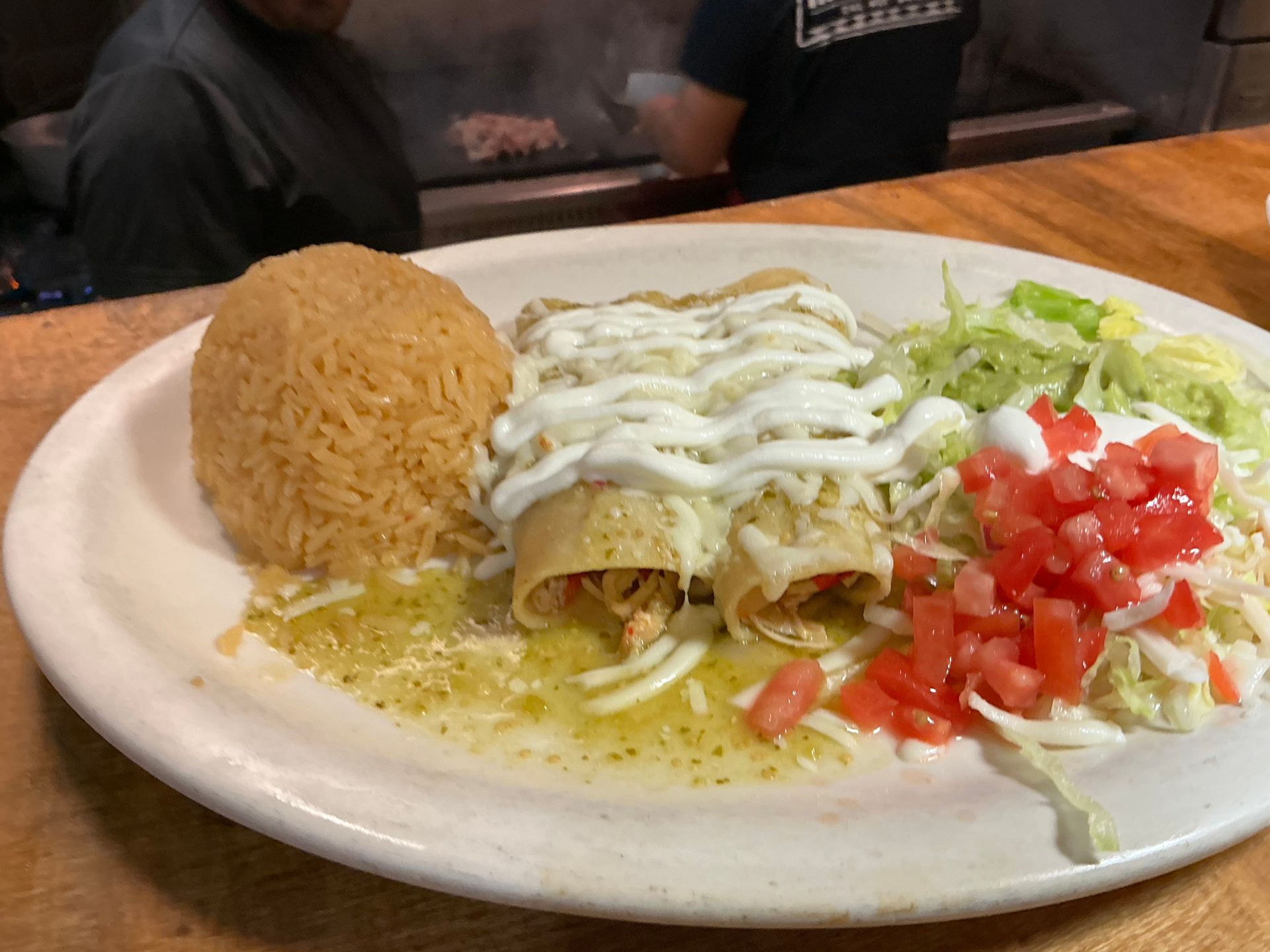 Plate of enchiladas with rice, lettuce, tomatoes, and sour cream.