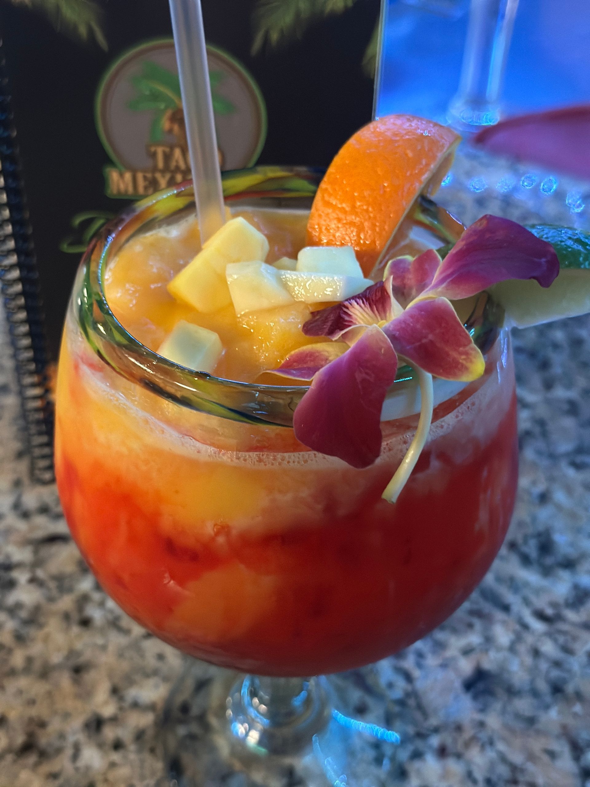 A colorful tropical cocktail in a glass with a flower and fruit garnish.