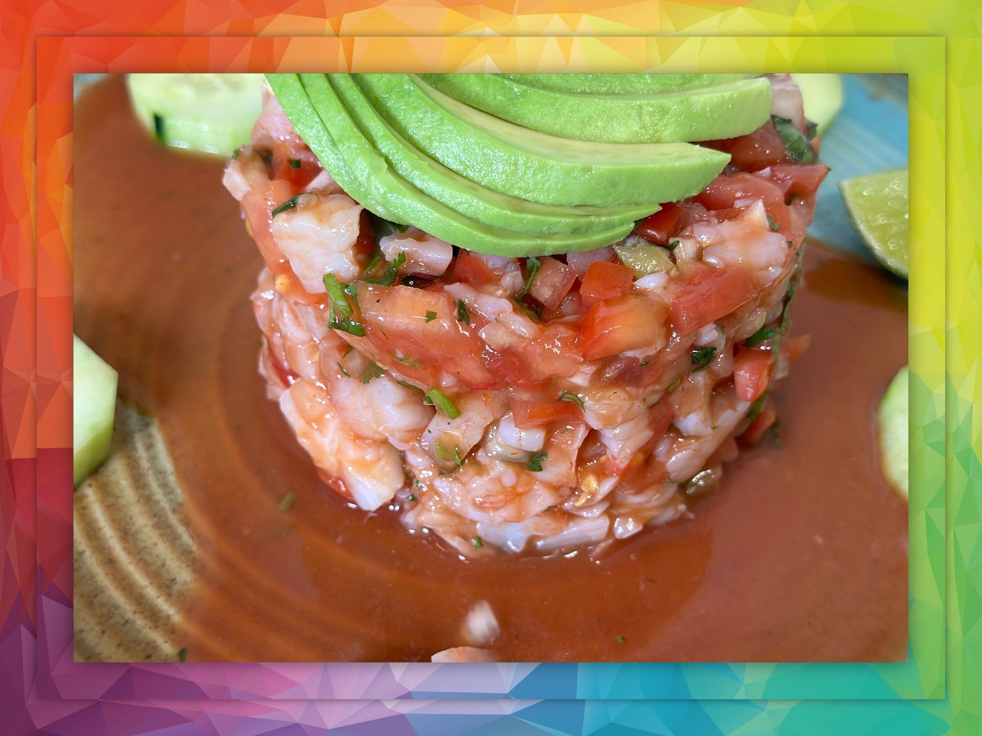 Shrimp ceviche with avocado slices, on a plate with brown sauce and lime wedges.