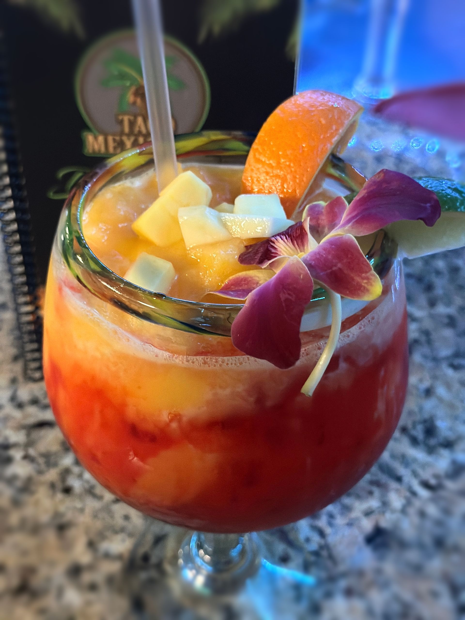 Tropical cocktail in a glass, layered orange and red, garnished with fruit and flower.