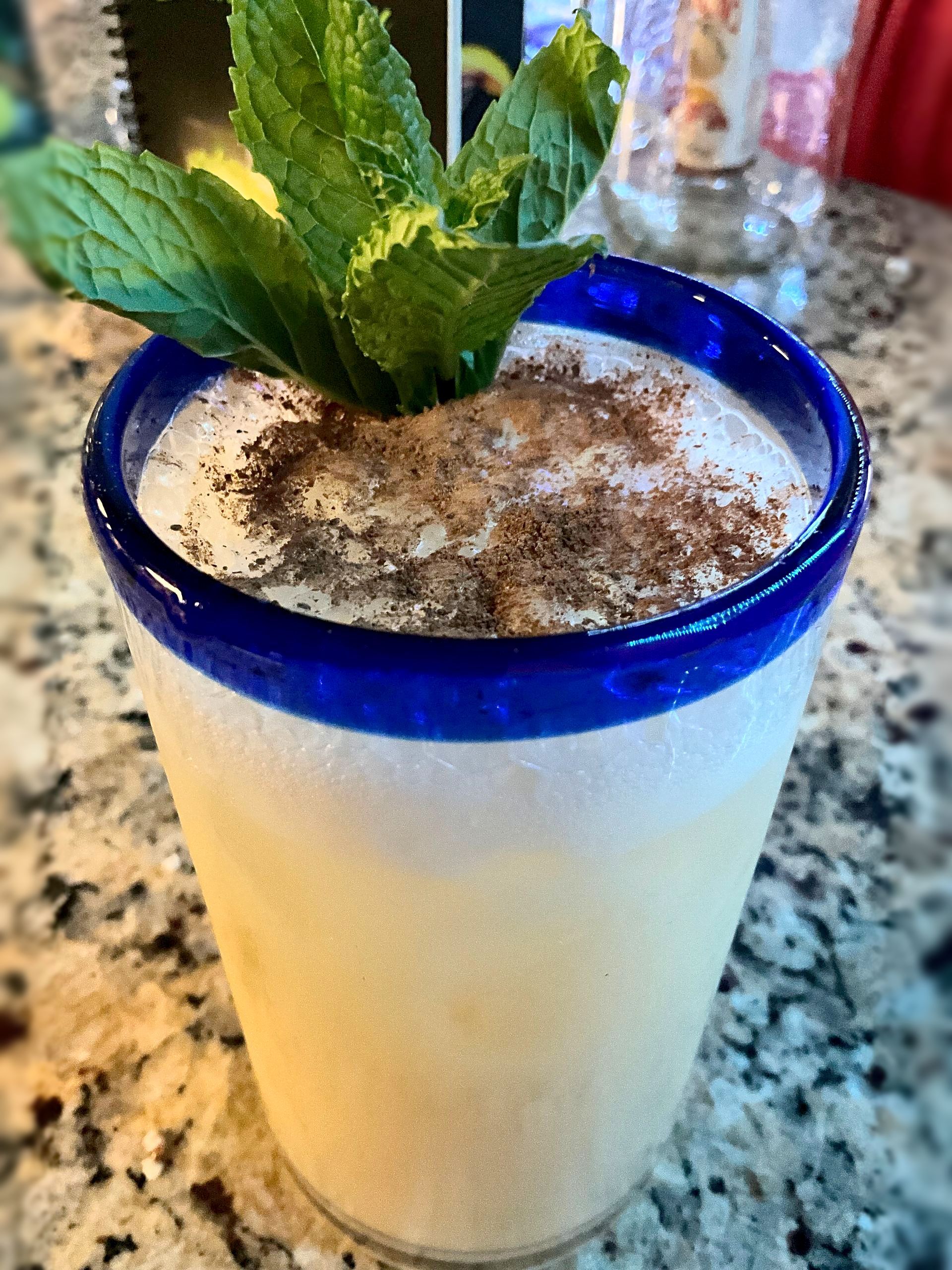 Frosted cocktail in a blue-rimmed glass, garnished with mint and cinnamon dusting.