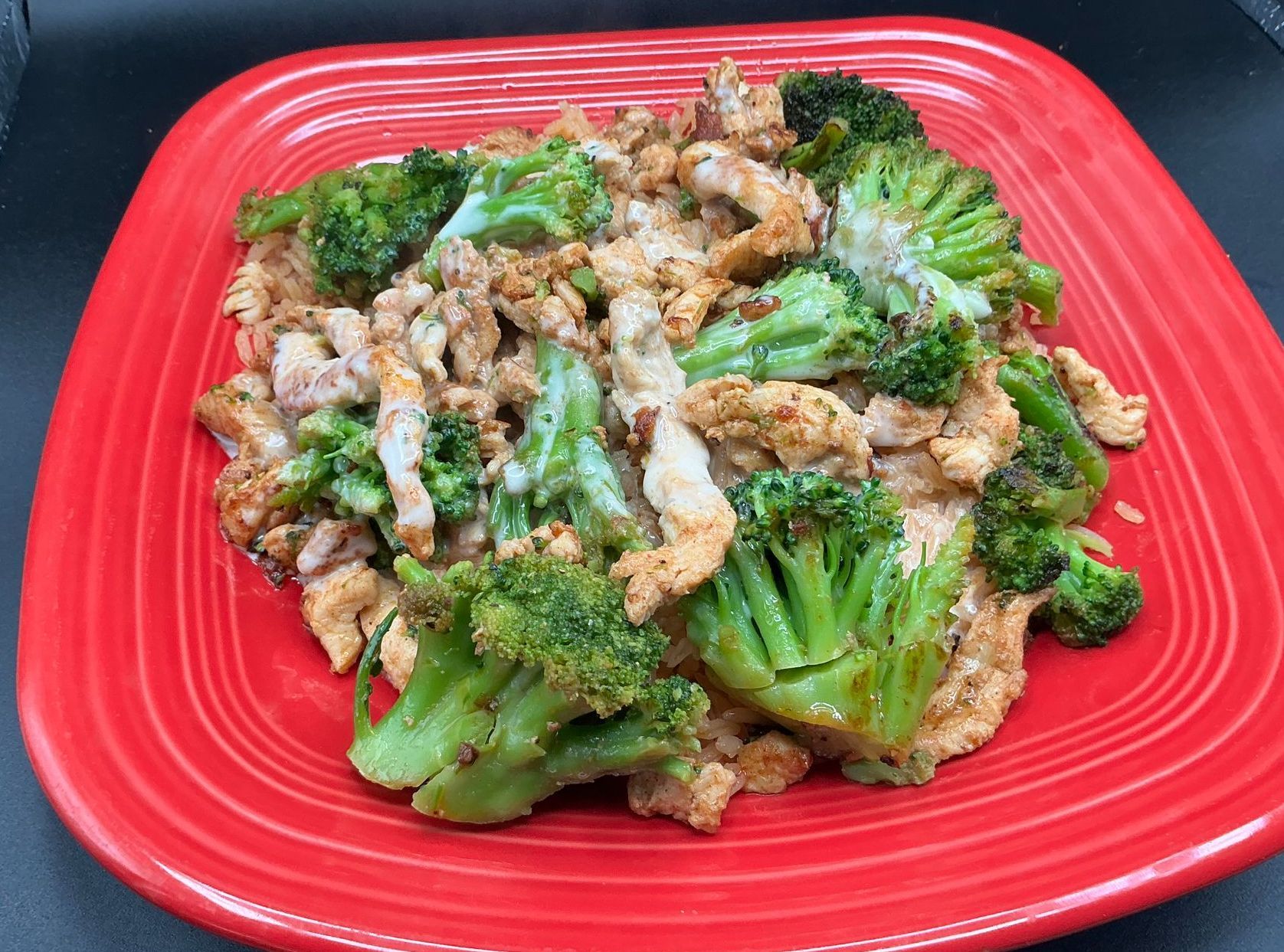 Chicken and broccoli stir-fry on a red plate. Broccoli florets and chicken pieces in a brown sauce.