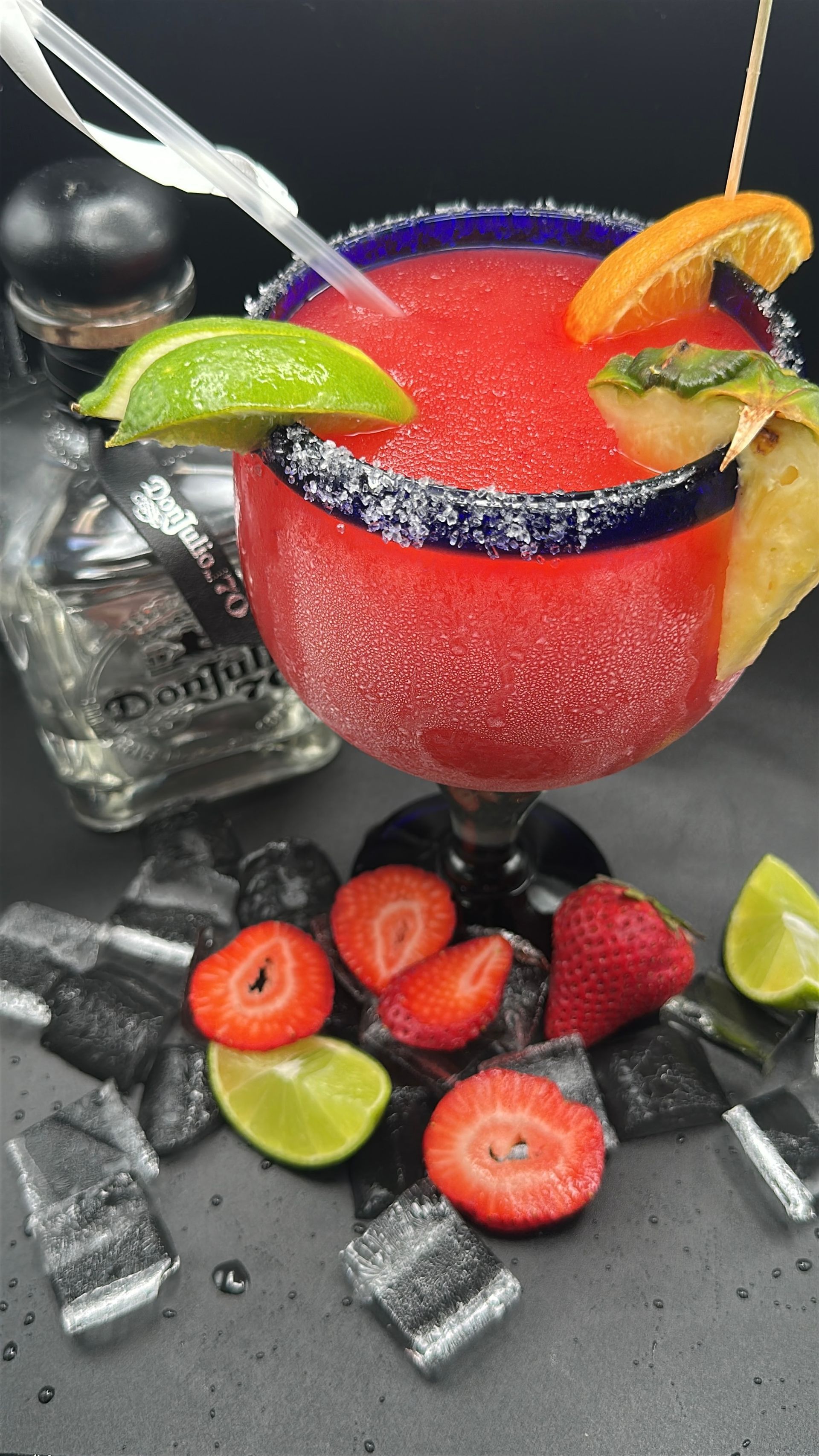 Strawberry margarita with lime, orange, and tequila on black surface.